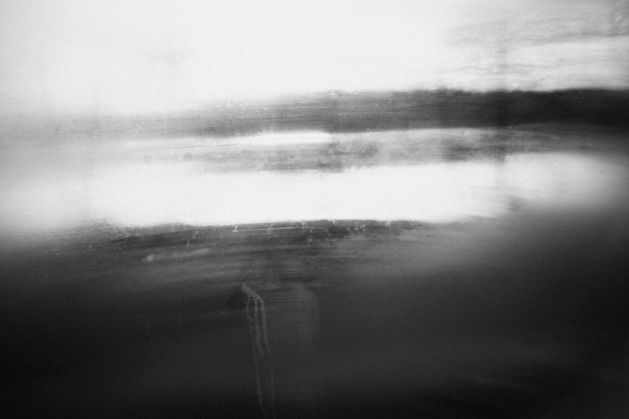 Mustavalkoinen kuva, jossa näyttää olevan epätarkka ja vääristynyt maisemakuva tai ovi/päivystys. Kuvassa on harmaita ja valkoisia sävyjä, mutta yksityiskohdat ovat epäselviä.