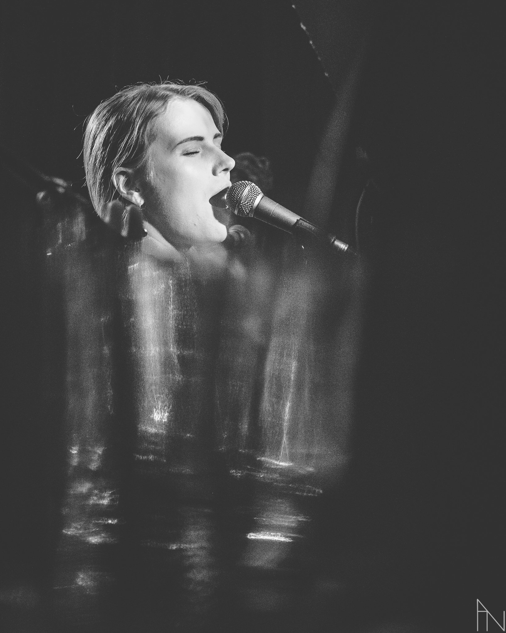 Musta-valkoinen kuva nainen laulamassa mikrofonin kanssa, hänellä lyhyt, vaalea tukka, suljetut silmät ja tunteella esiintyvä.