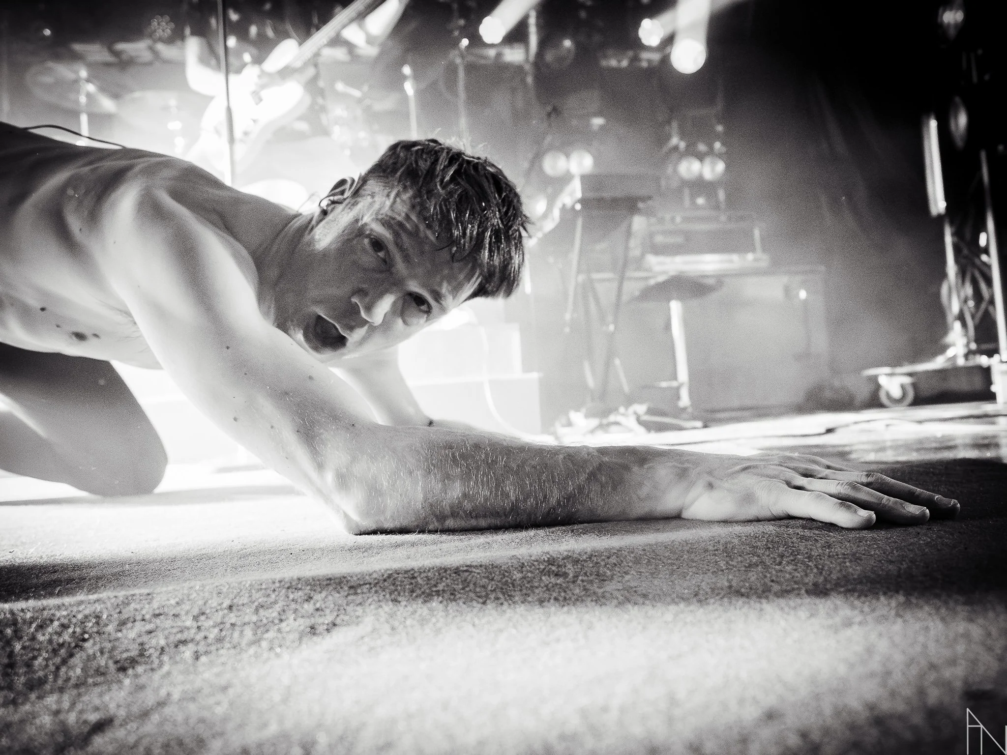 Mies polvillaan esiintymislavalla, katsoo suoraan kameraan ja näyttää voimakkaalta ilmaisulta.