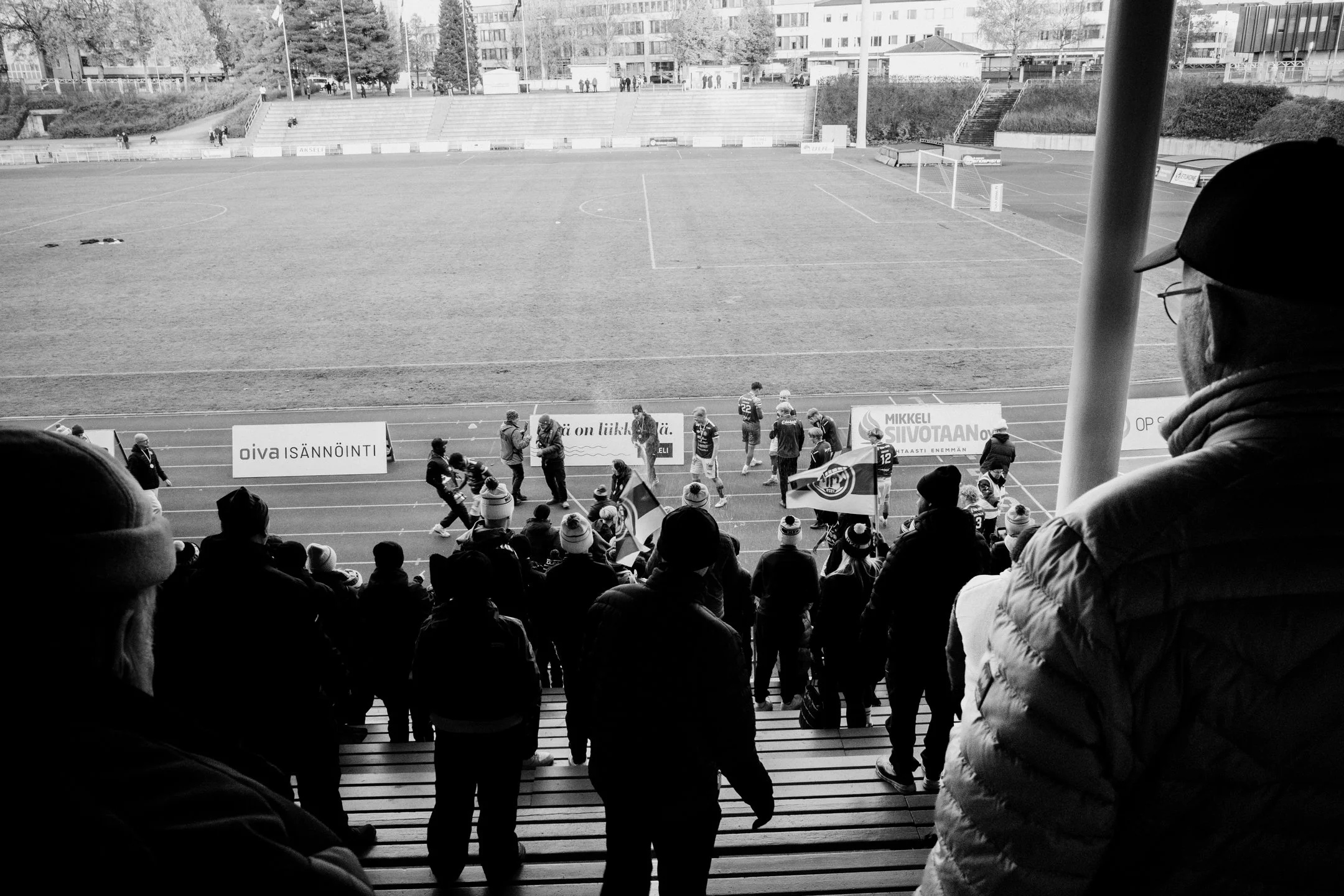 Mustavalkoinen kuva stadionilta, joissa ihmiset seisovat katsomon portailla ja juoksuradalla. Joitakin ihmisiä pitelemässä lippuja ja katsojia katsomossa.