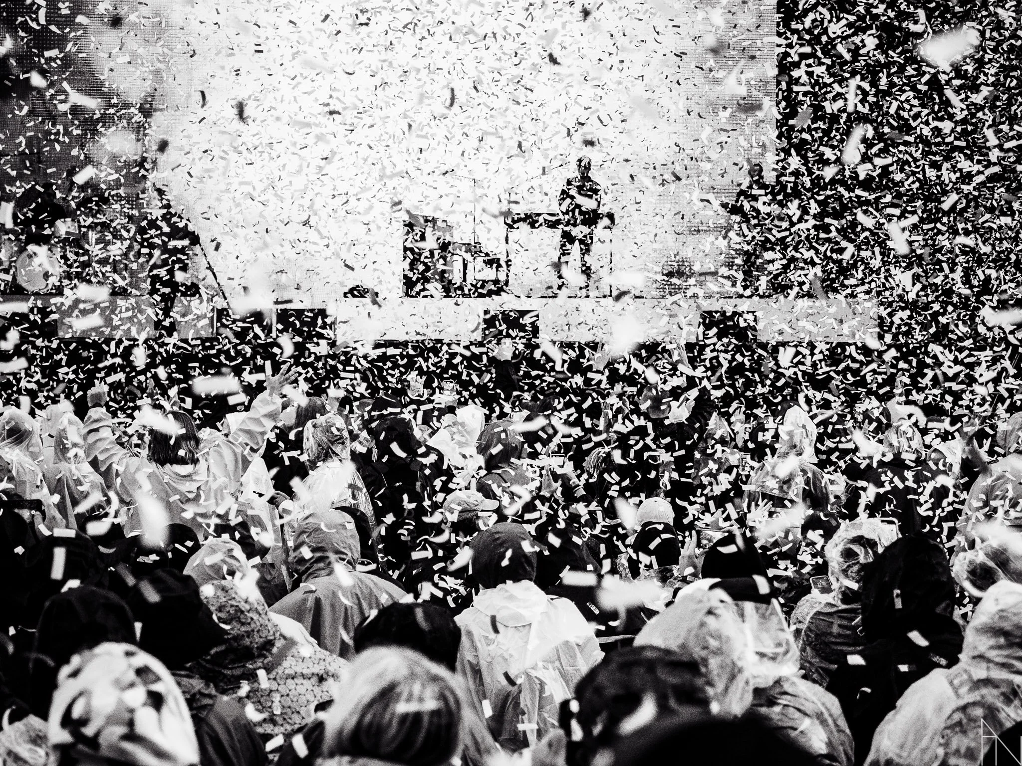 Suuri ihmisjoukko, päällä sadevaatteet, juhlii tai katsomassa tapahtumaa, kun konfettia lentää ilmassa.