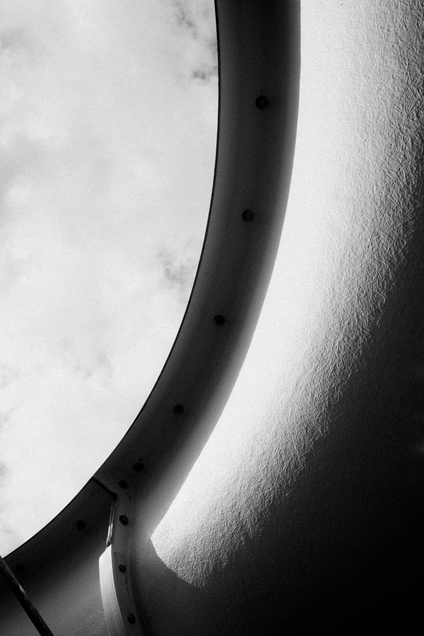 Mustavalkoinen valokuva ikkunasta, jossa on metallinen kehys ja näkymä pilviseen taivaaseen.