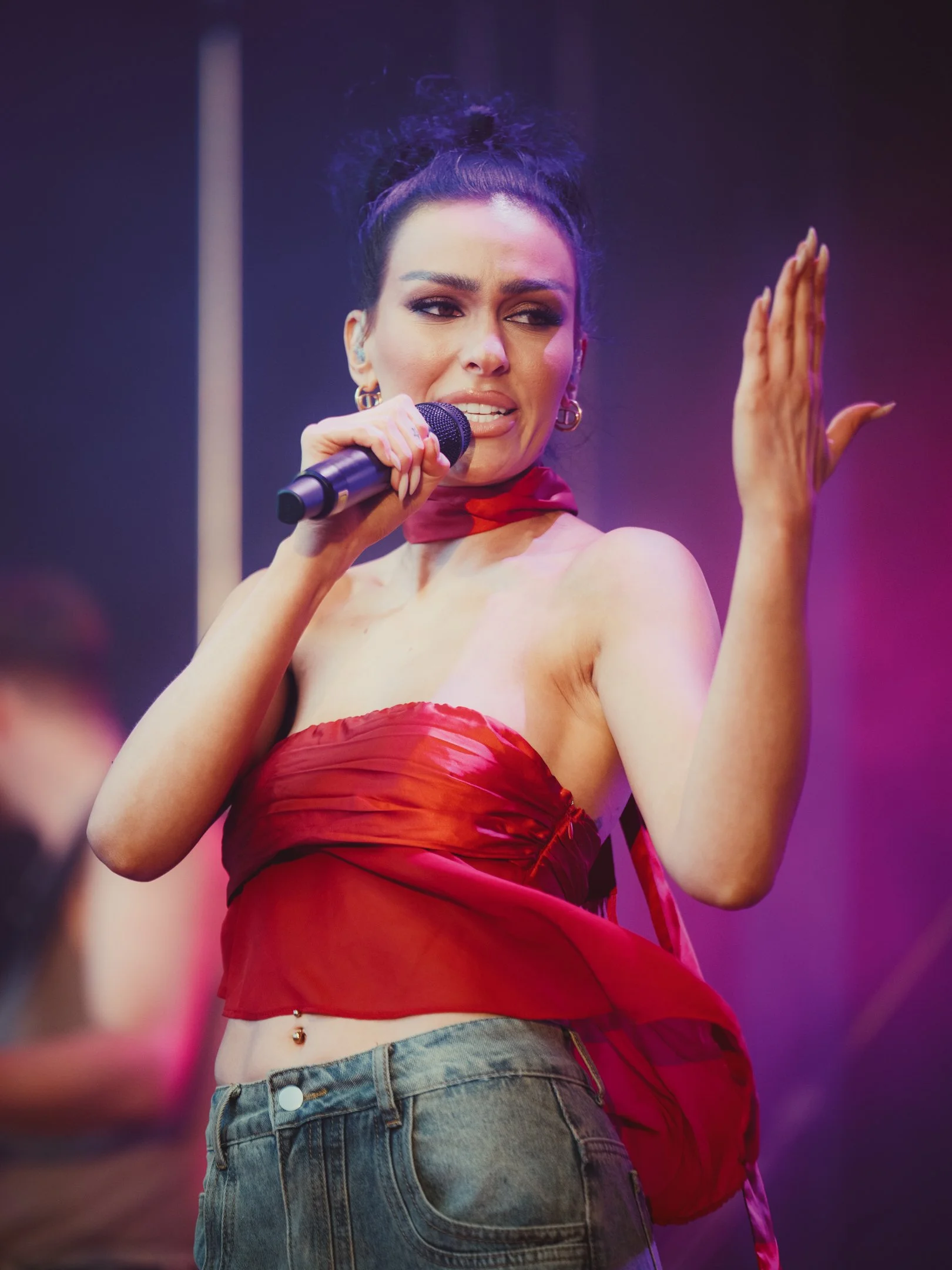 Nuori nainen, Sara Siipola, laulamassa mikrofonilla, taustavaloja ja esiintymisympäristö.