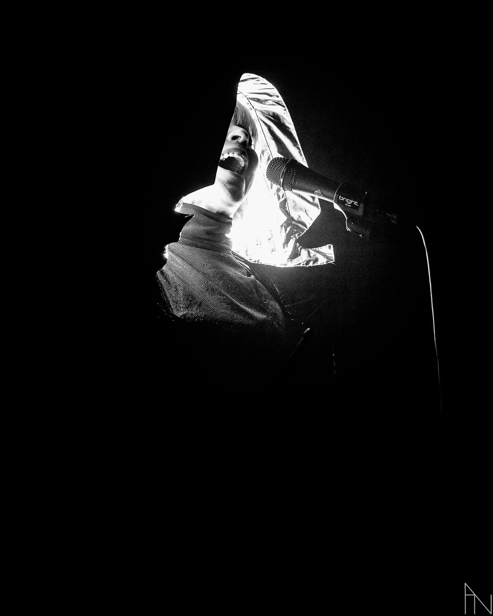 Valkoinen-huivi päässä oleva nainen laulamassa mikrofonin edessä, taustalla valkoinen ja musta.