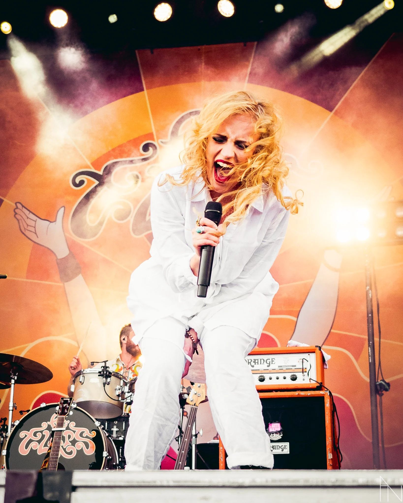 Elli Haloo laulamassa mikrofoniin konserttilavalla, taustalla bändi ja kirkas valoshow.