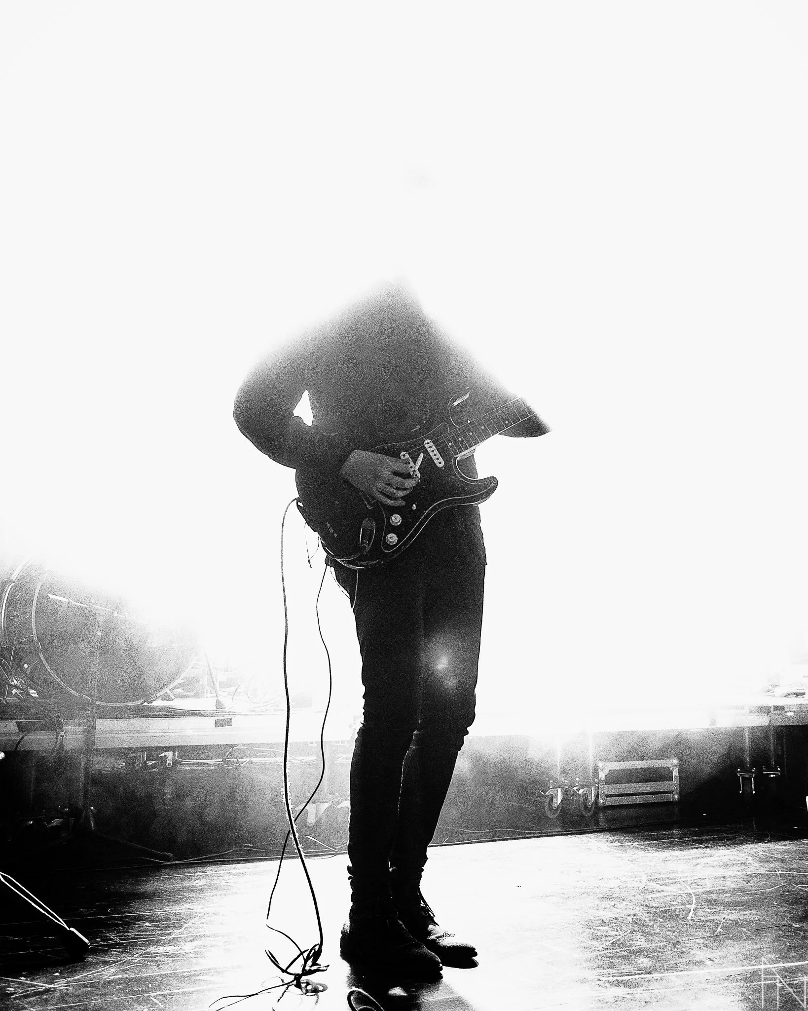 Mies soittaa sähkökitaraa lavalla, taustavalo ja savuke ovat läsnä, mustavalkoinen kuva.