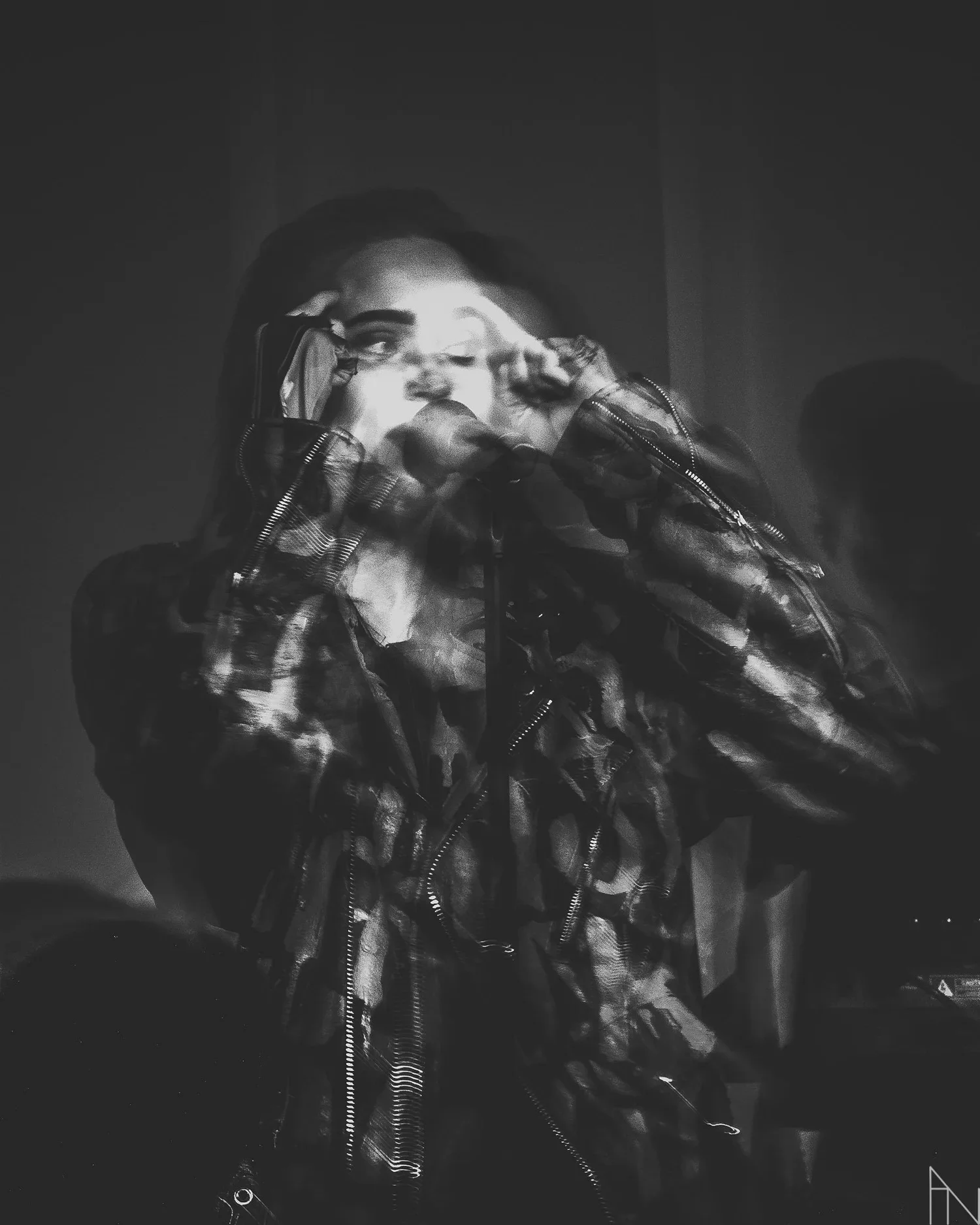 Mustavalkoinen kuva naisesta, joka käyttää nahkatakkia ja liikkuu nopeasti, luoden liukuvan efektin. Hänellä on panta tai hiuskoriste ja taustalla näkyy toinen henkilö.