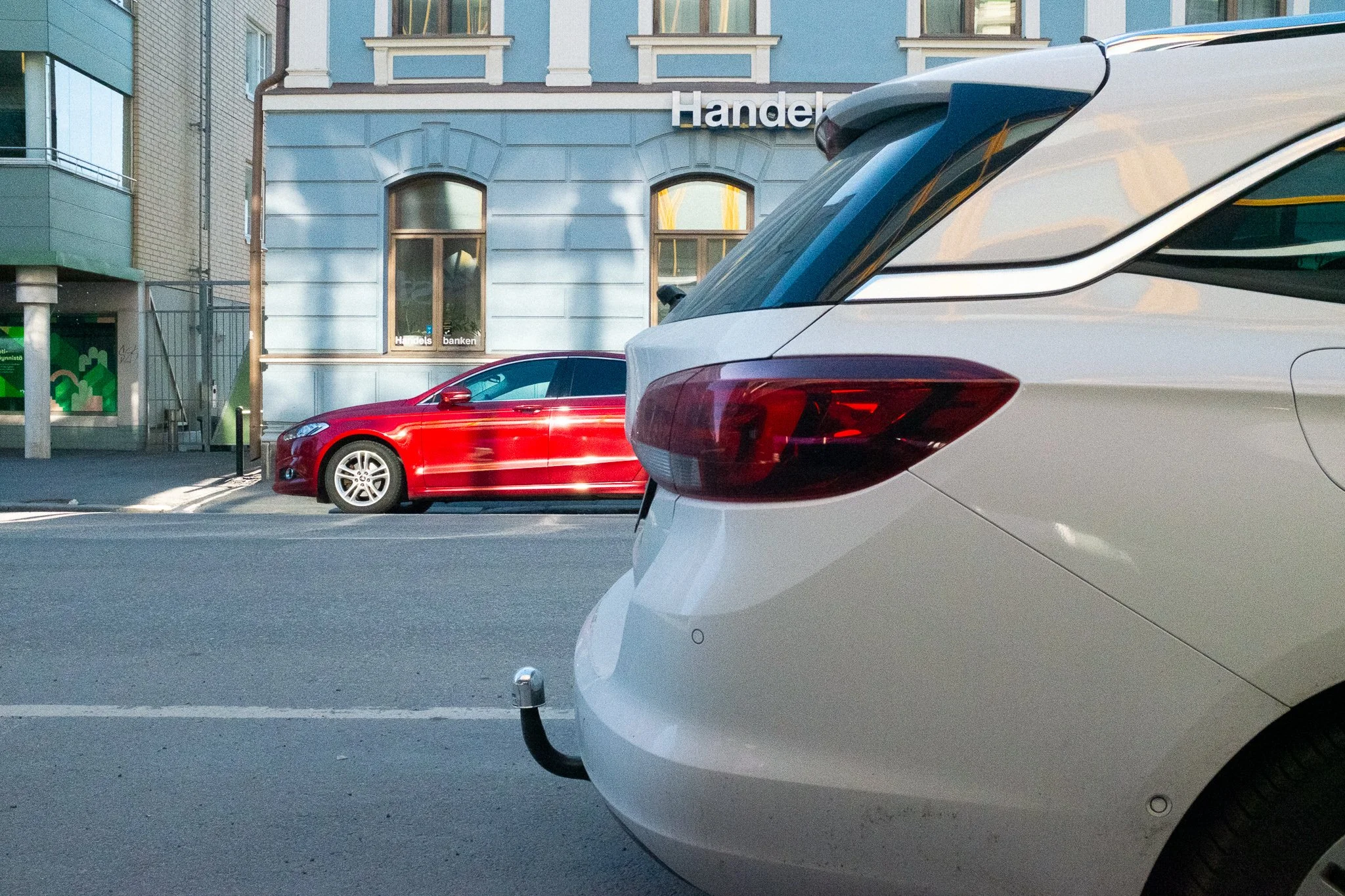 Kaksi autoa pysäköitynä katupysäköintitilassa, taustalla vanha rakennus ja liikennemerkki.