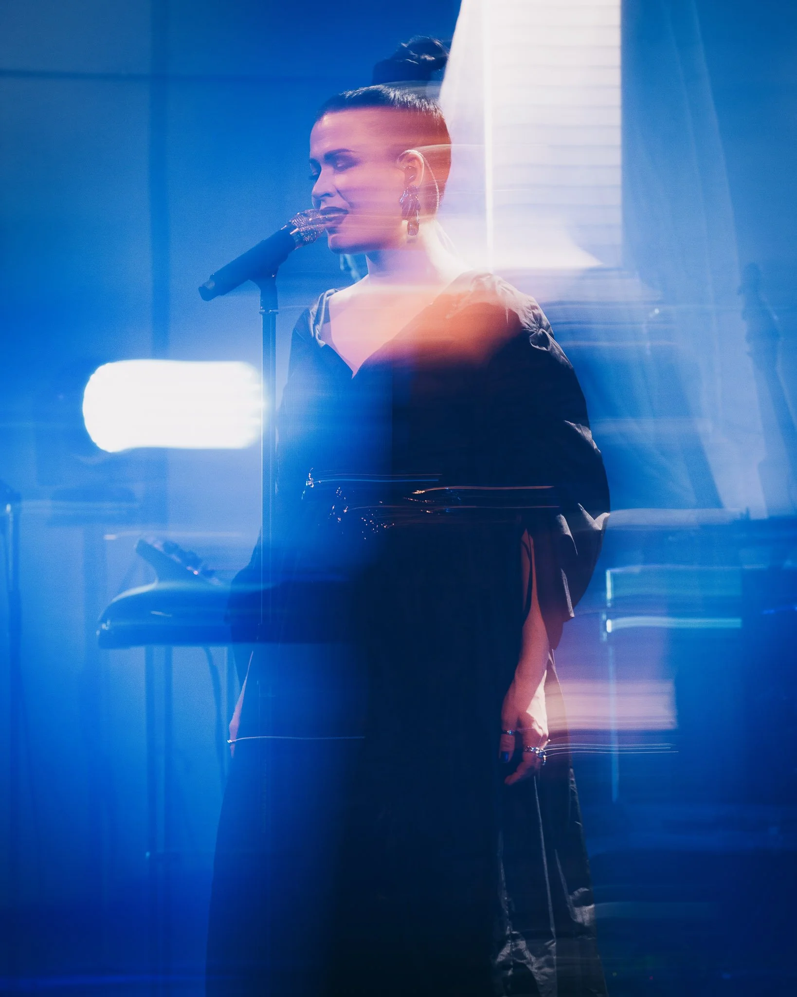 Nainen laulaa mikrofonin kanssa pimeässä, valot ja heijastukset luovat abstract-efektin.