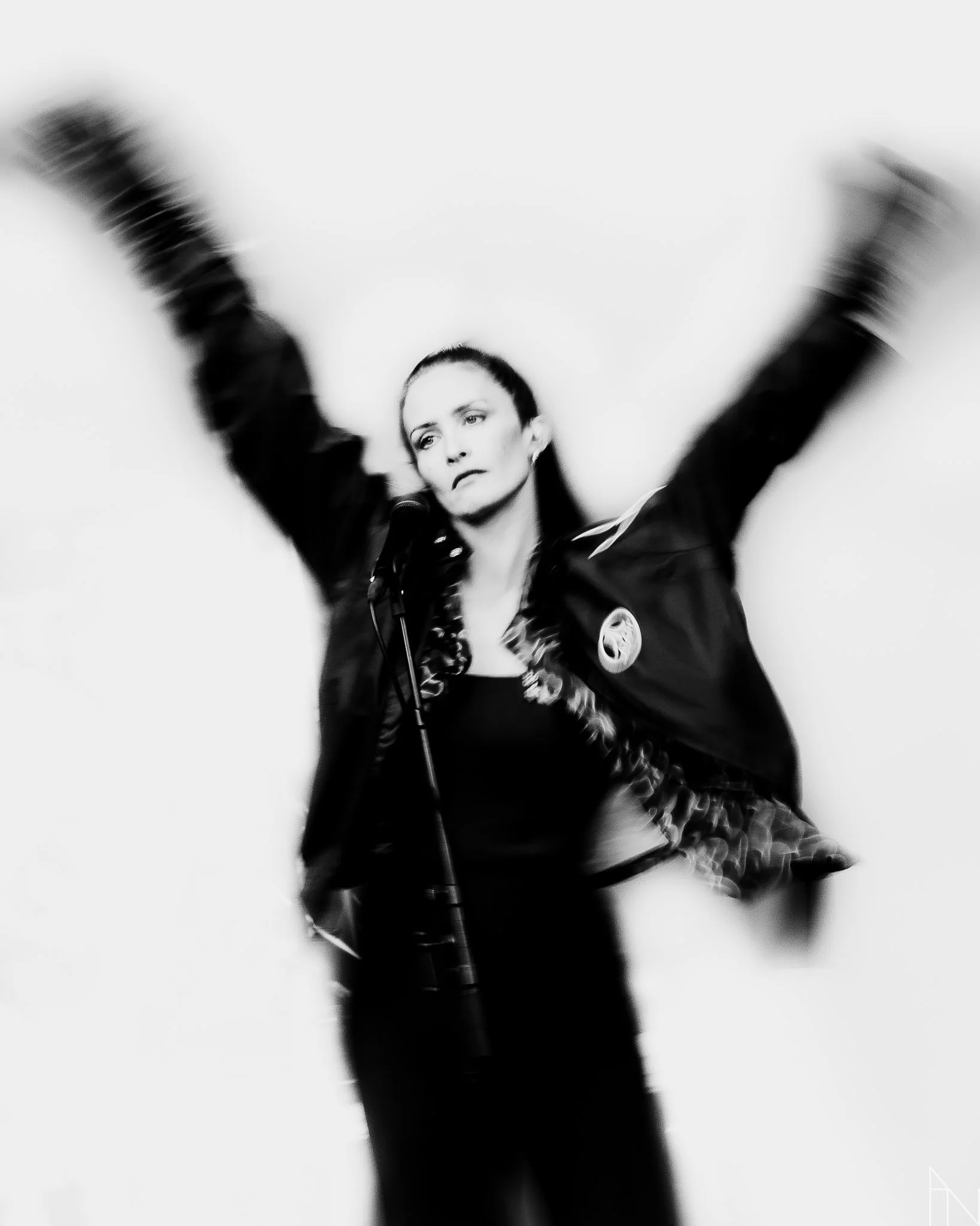 Mustavalkoinen kuva nainen, joka seisoo mikrofonin edessä ja liikkuu vilkkaasti, kädet ilmassa.