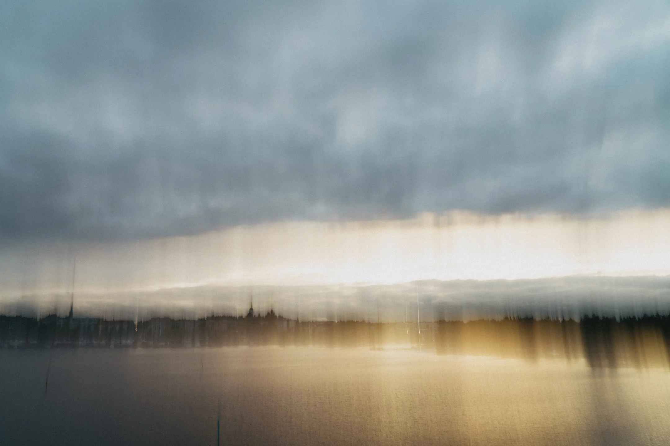 Tummat pilvet peittävät horisonttia ja auringonvalo heijastuu veteen, luoden esteettisen maiseman.