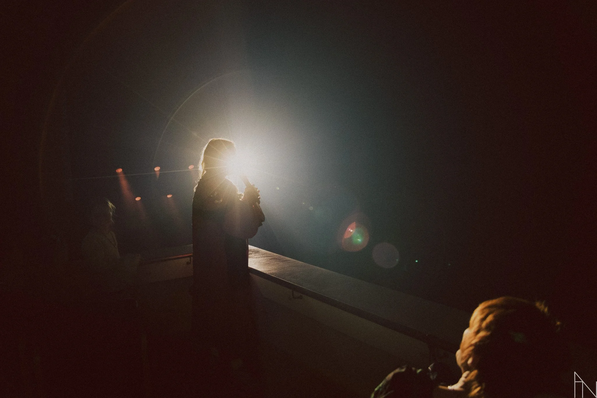 Henkilö laulaa mikrofonia käsissään, taustalla valoisteita ja muita ihmisiä, joissa on pimeä.