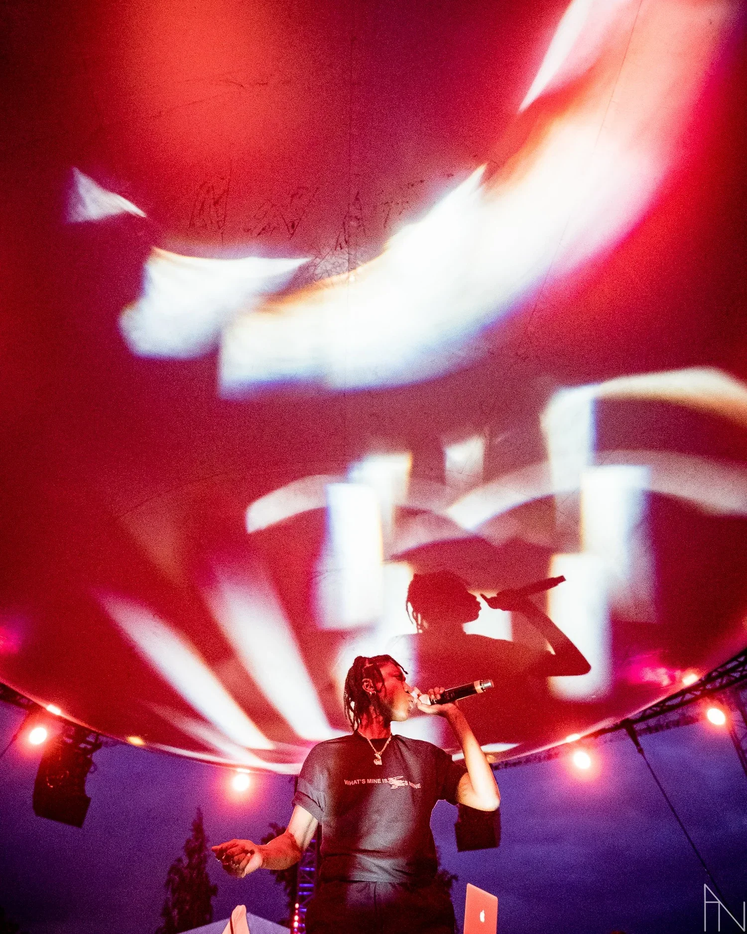 Nainen esiintyy lavalla mikrofonin kanssa, taustalla valojen ja projektioiden muodostama varjo hänestä.