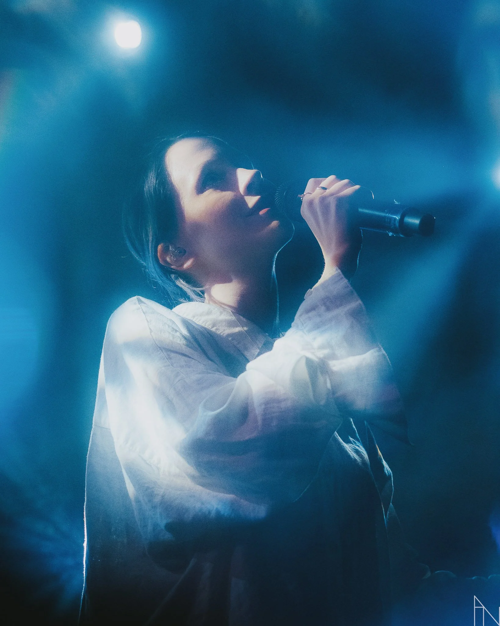 Nainen, Pehmoaino, laulaa mikrofonin kanssa lavalla, taustalla sininen valaistus. Lutakko 2022.