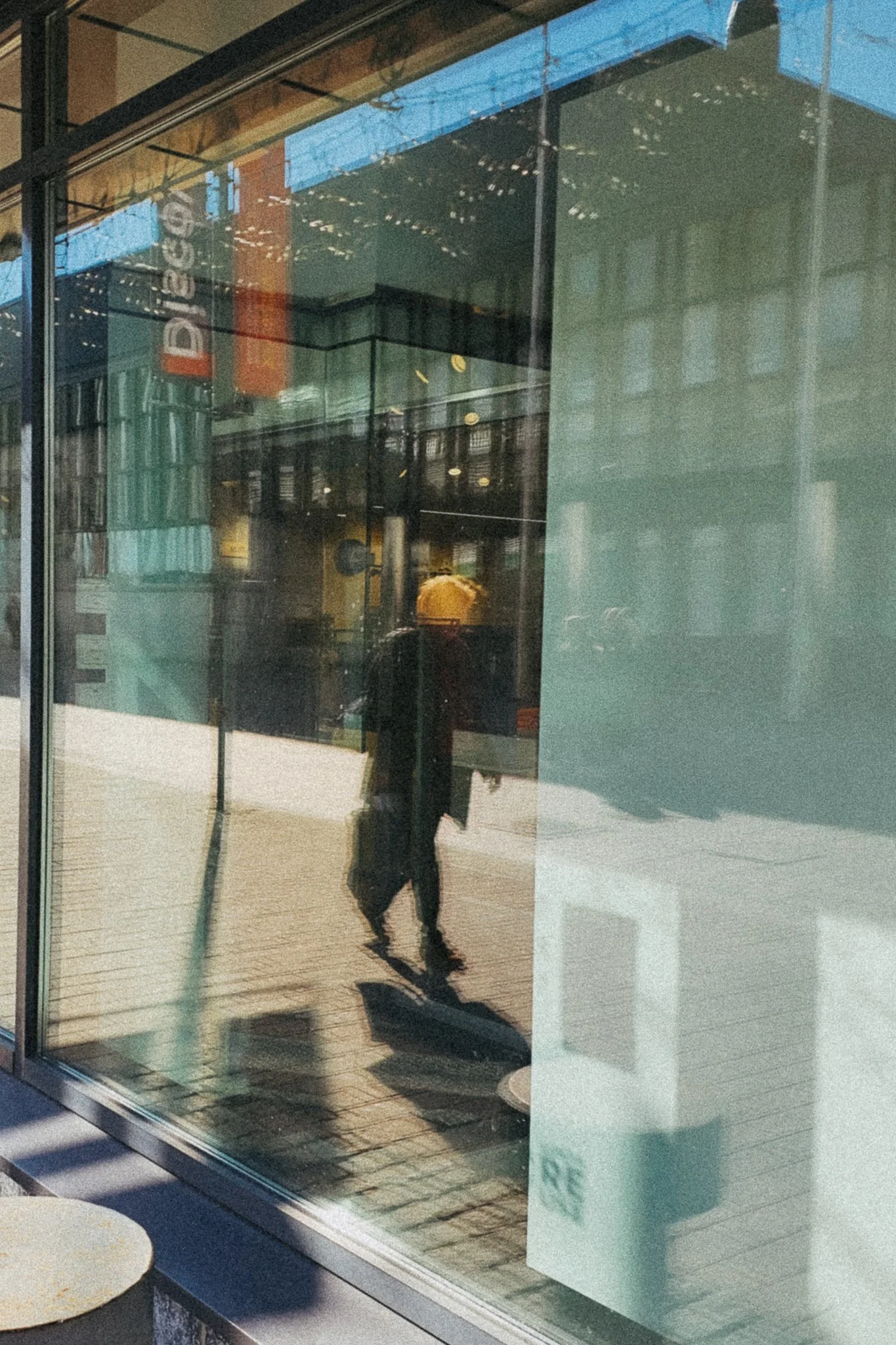 Heijastuva kuva kaupunginkäytävästä, jossa näkyy henkilö kävelemässä ja kauppojen ilmakyltti.