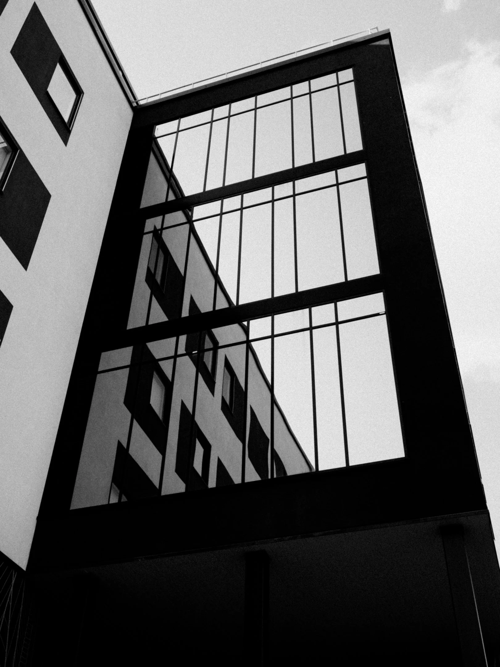 Kuvassa on moderni rakennus, jossa on suuri lasiseinä ja mustat kehykset, ja osa rakennuksesta on näkyvissä taivasta vasten.