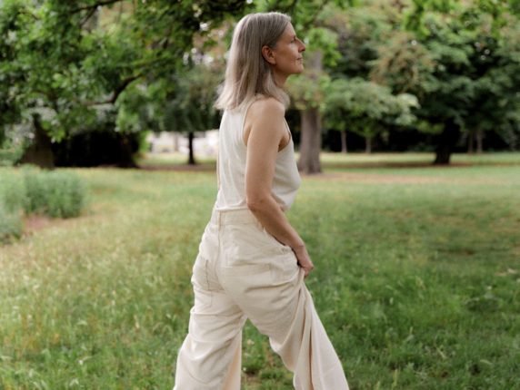 A woman in her late fifties wearing a white outfit, walking in a beautiful green park.