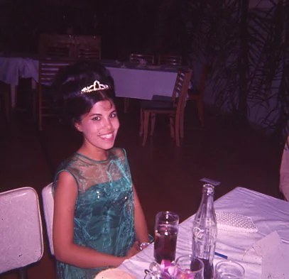 A young girl in a green dress with a tiara sitting at a table during a celebration or party.