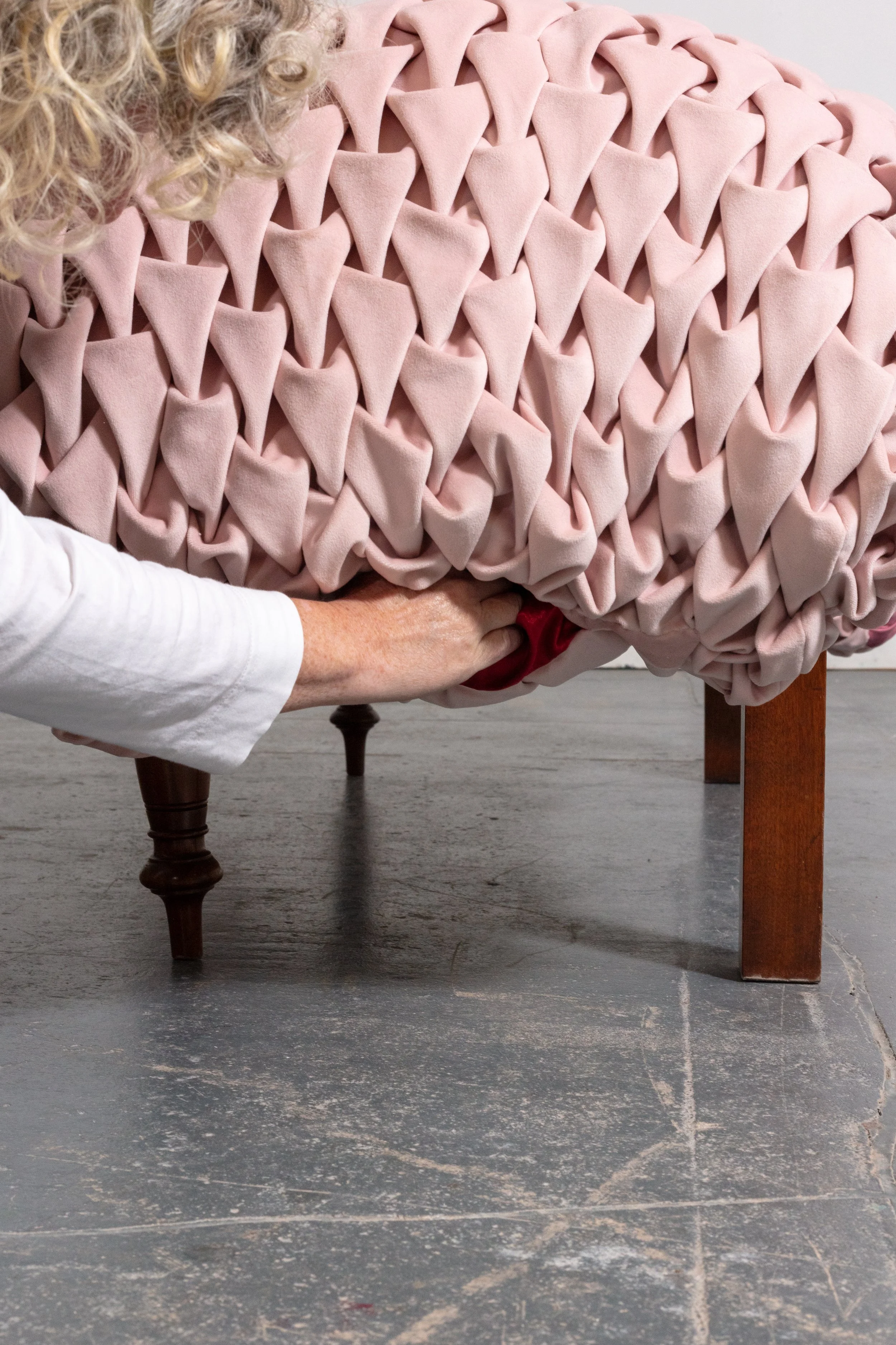 Close-up of a pink textured blanket with a diamond-like pattern, draped over a wooden chair with a dark finish in a room with a concrete floor.