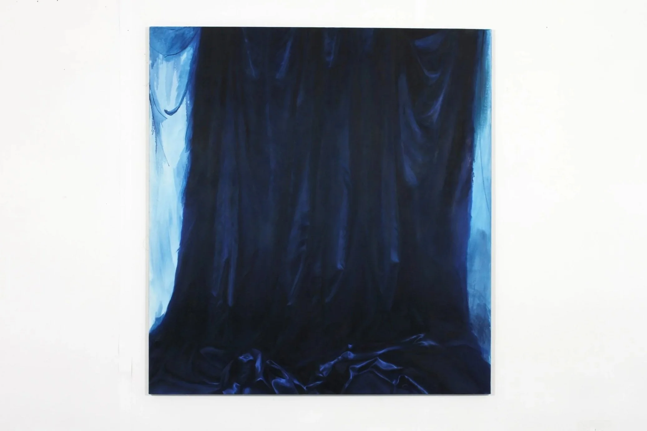 A large painting of dark blue and black fabric with shadows and folds, mounted on a white wall.