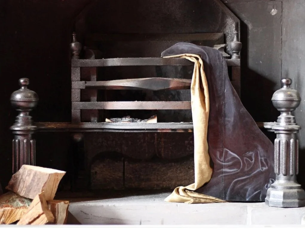 A vintage fireplace with a metal grate, a rolled-up blanket or cloth, and some firewood on the hearth.