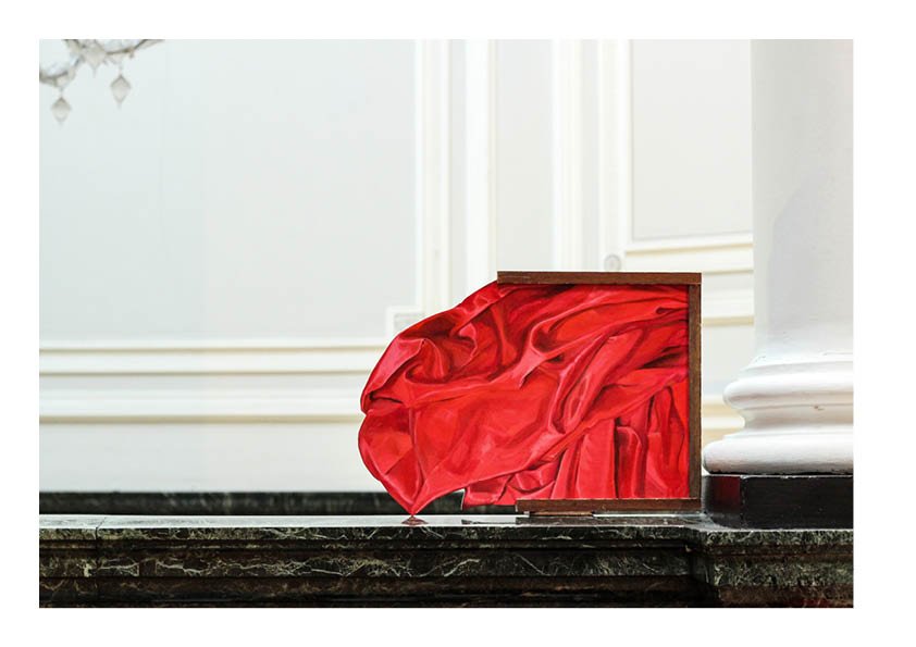 A mirror partially covered by red satin fabric on a dark marble surface in a white room.