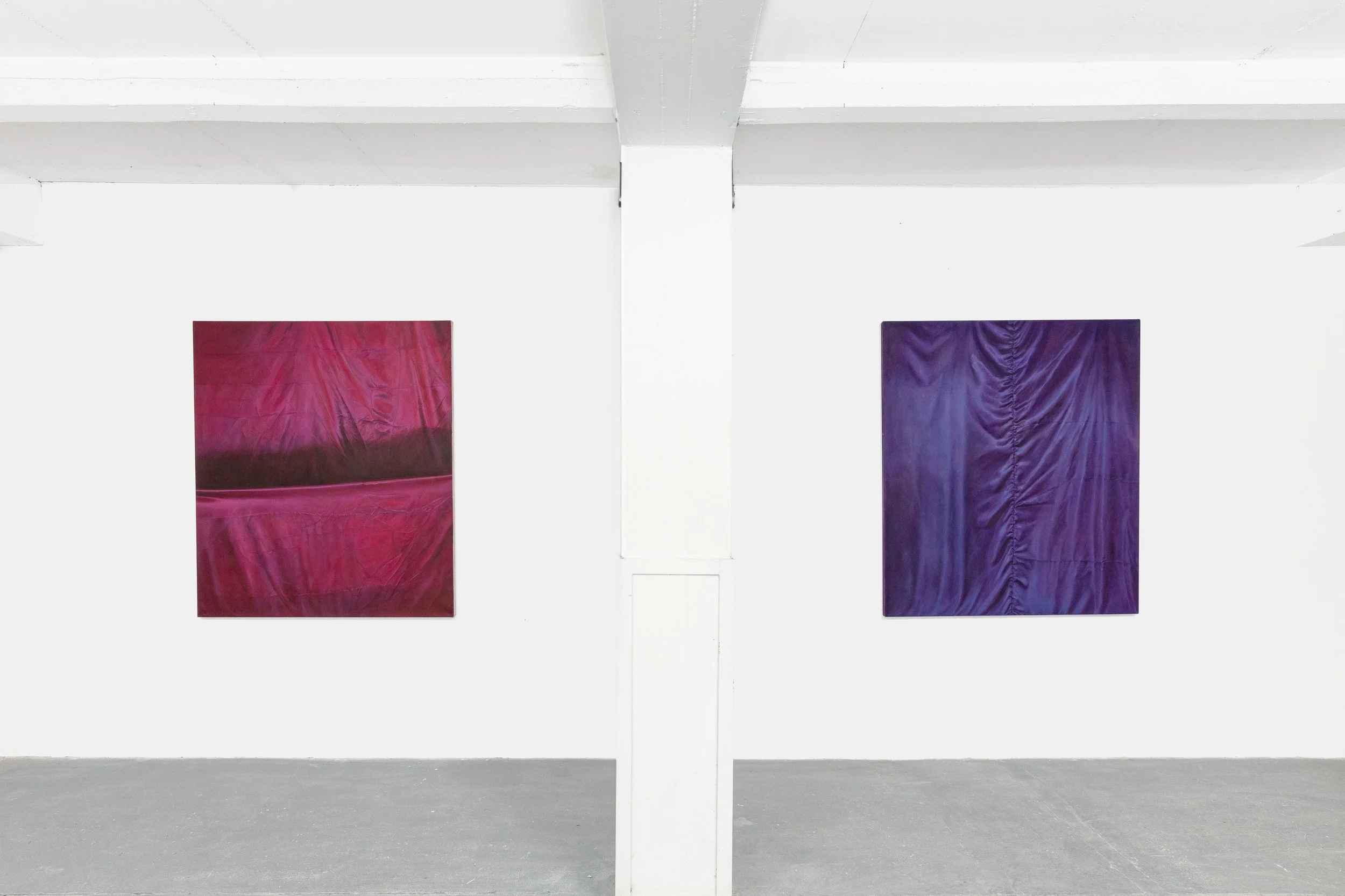 Two square abstract paintings, one red and one purple, mounted on a white gallery wall with a white support column in the center.