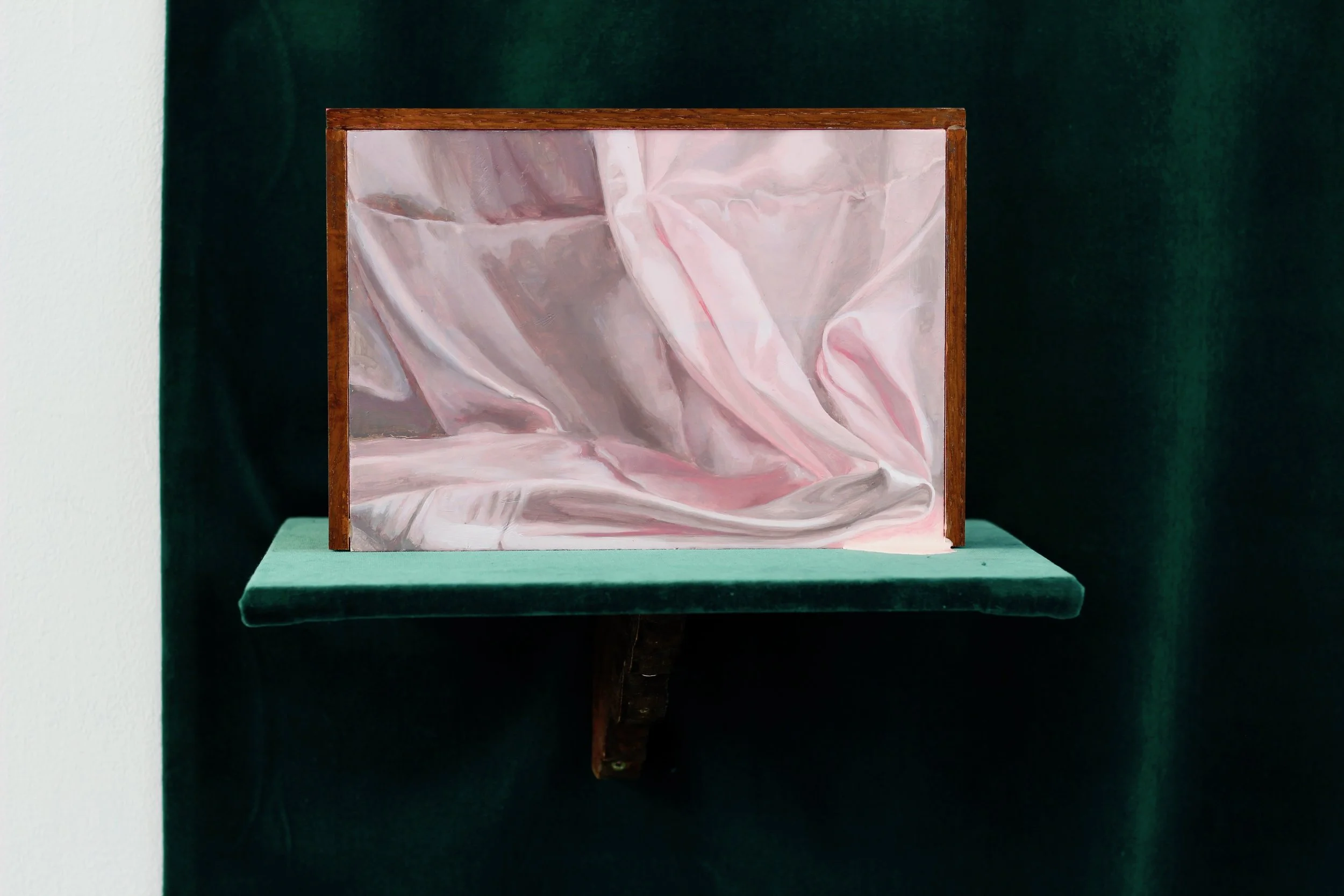 Painting of pink and white crumpled fabric displayed on a shelf with a dark green background.