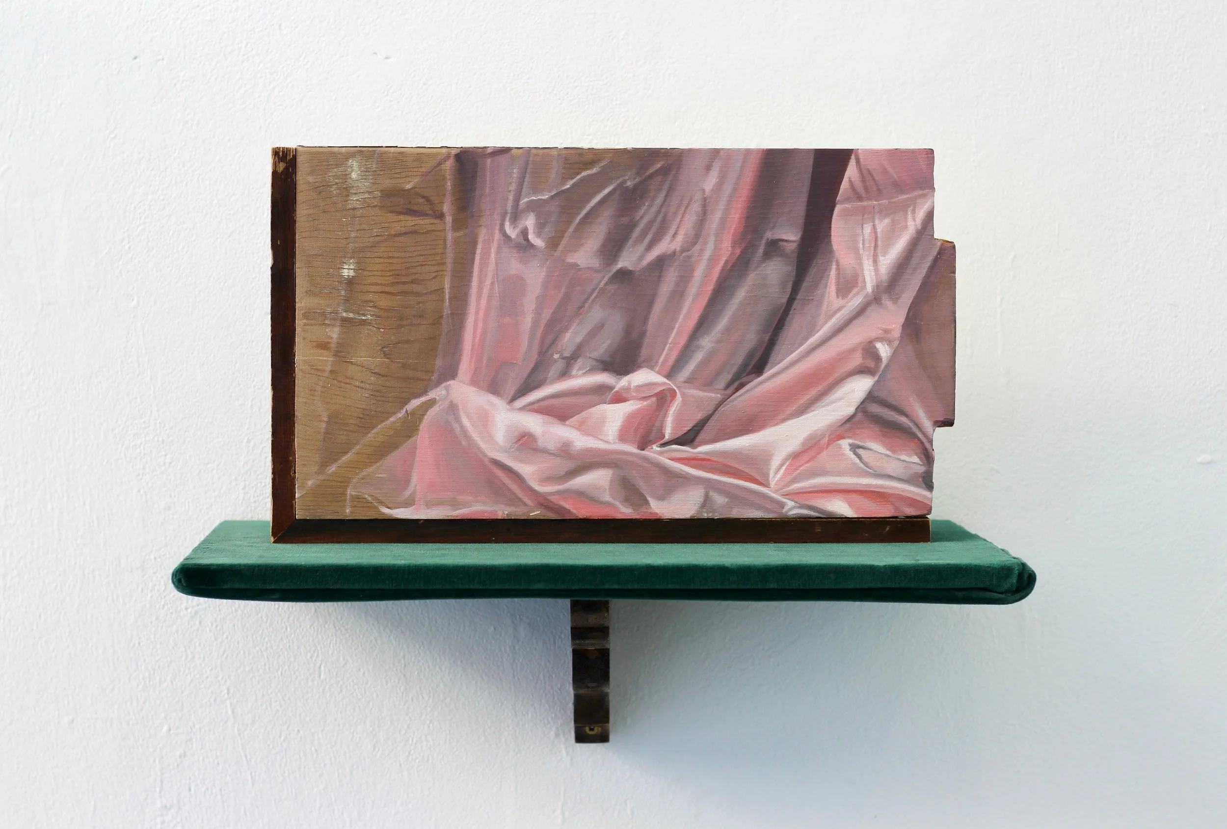 A painting of pink and gray fabric with folds, mounted on a wooden panel, displayed on a green stand against a white wall.