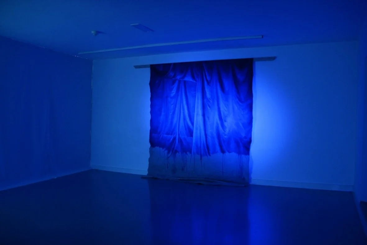 A room illuminated with blue light, featuring a window with curtains.