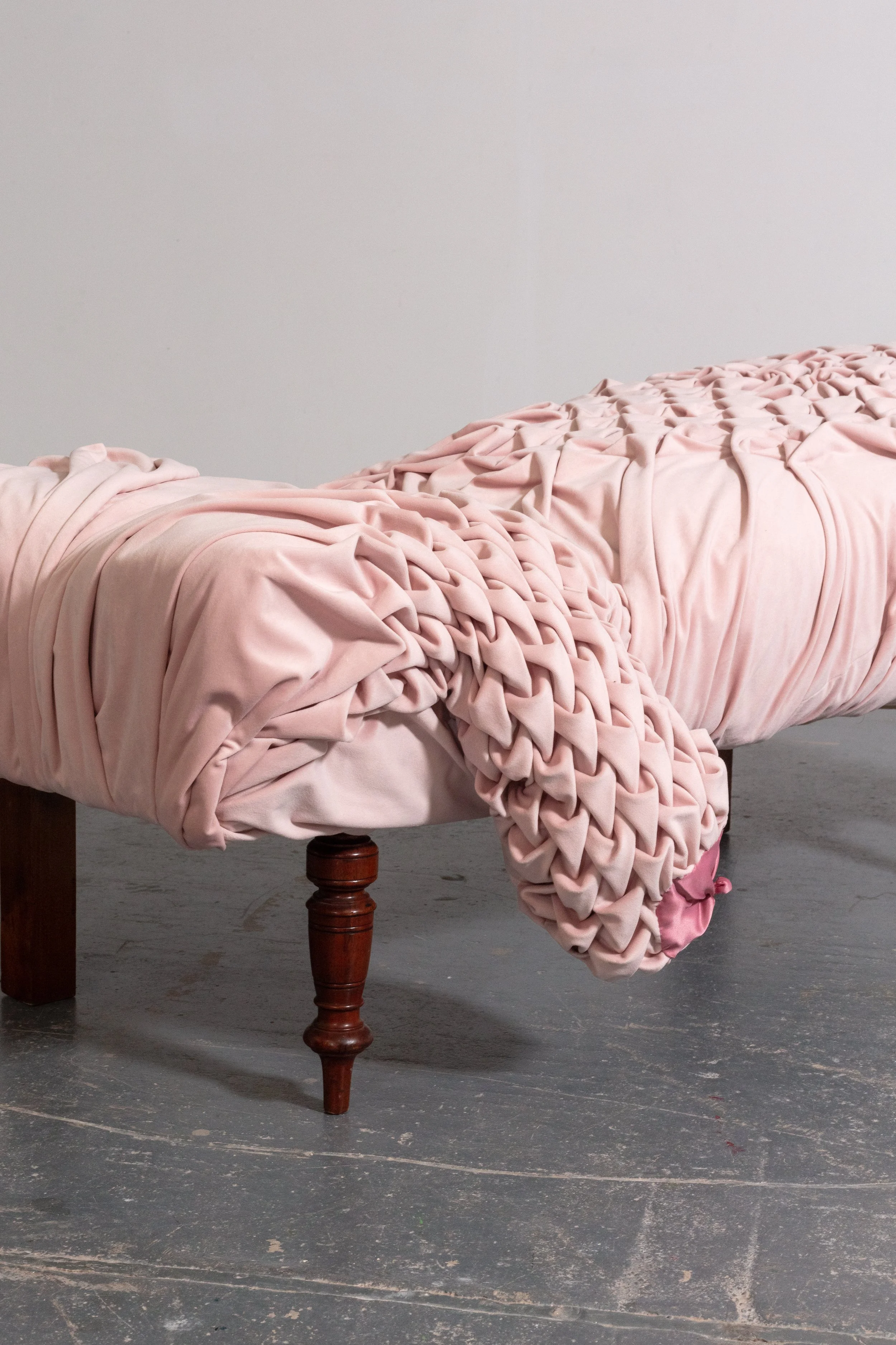 A rustic wooden table with a large, pink, ruffled fabric draped over the edge, set against a plain white wall and gray concrete floor.