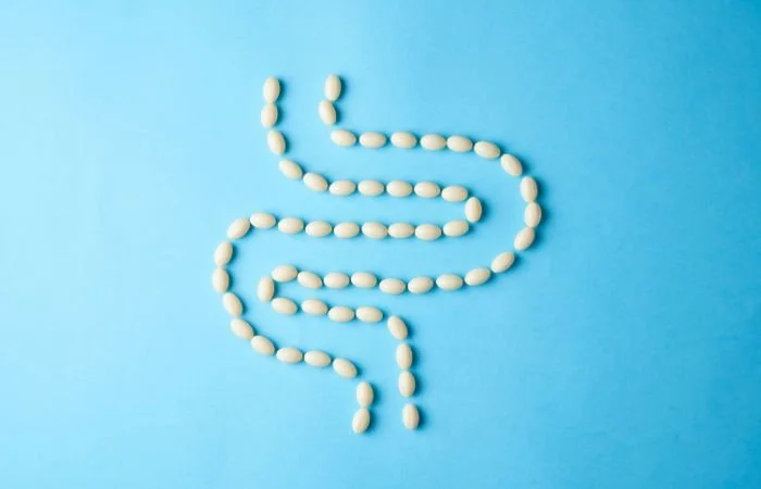 Probiotic capsules arranged in the shape of a digestive tract, on a blue backdrop.