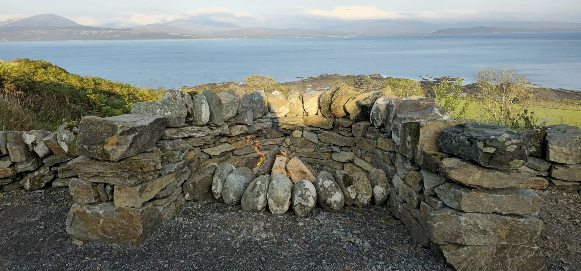 A stone fire pit with a view of a lake, mountains, and green landscape in the background.