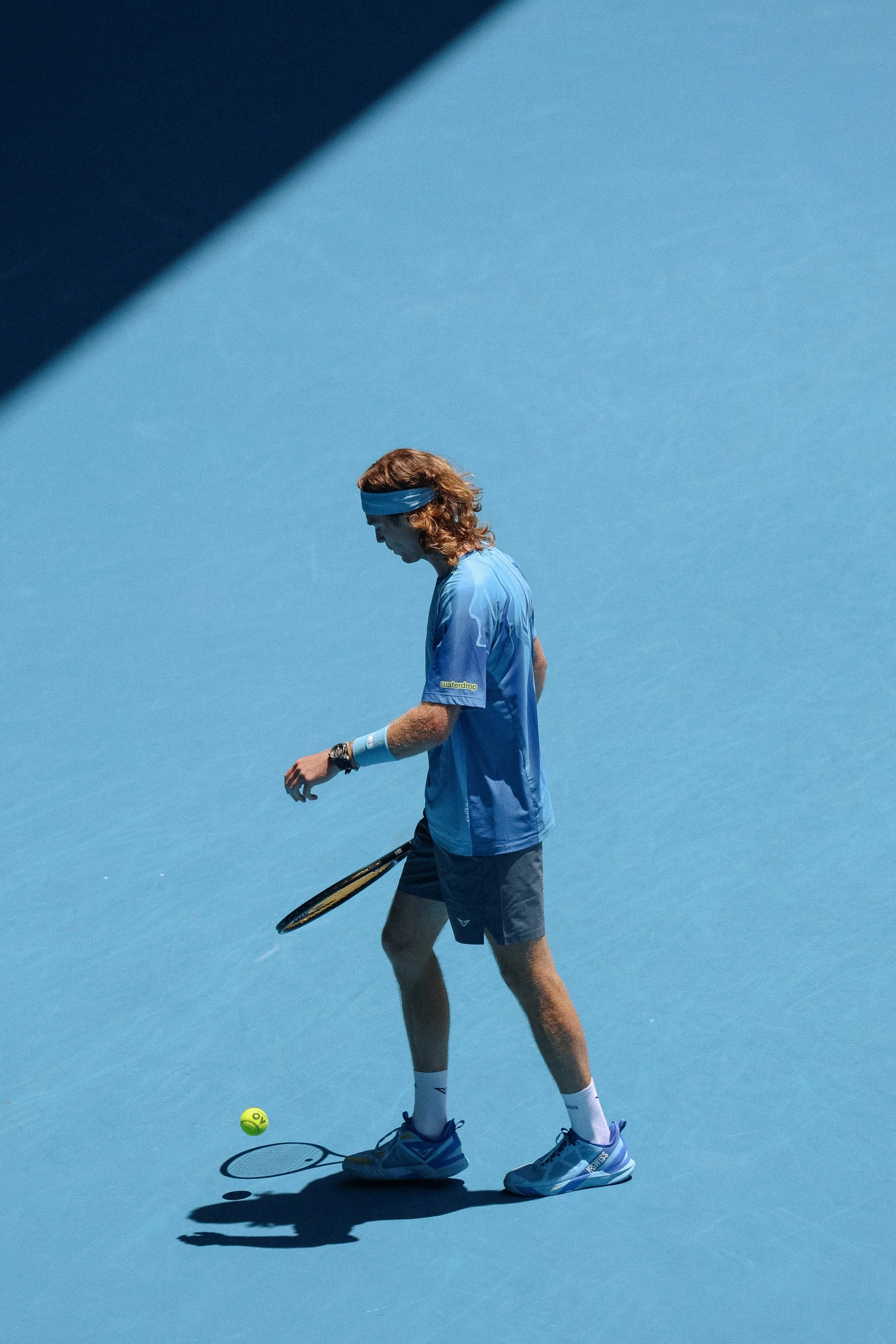 A male tennis player dressed in blue on a blue tennis court, preparing to hit a tennis ball.
