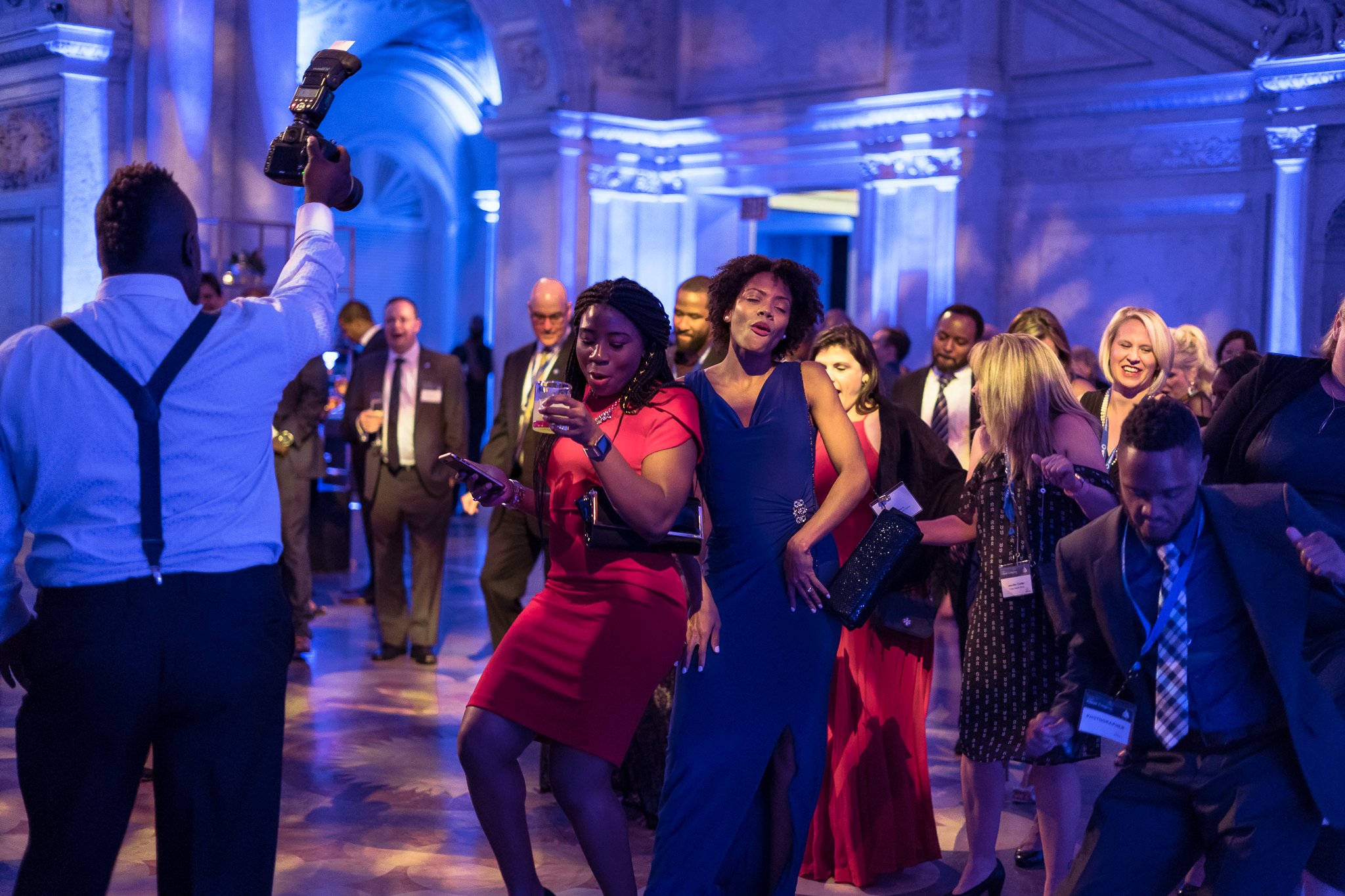People dancing and socializing at a formal event in a decorated ballroom with blue lighting.
