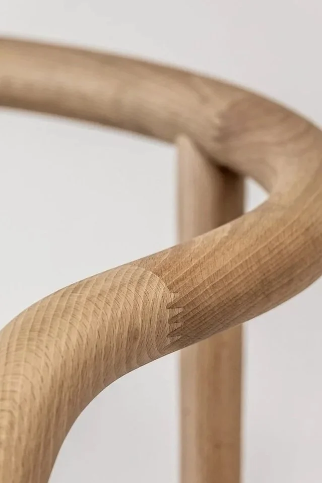 Close-up of a wooden chair's curved armrest showing a finger joint with a smooth, natural finish.