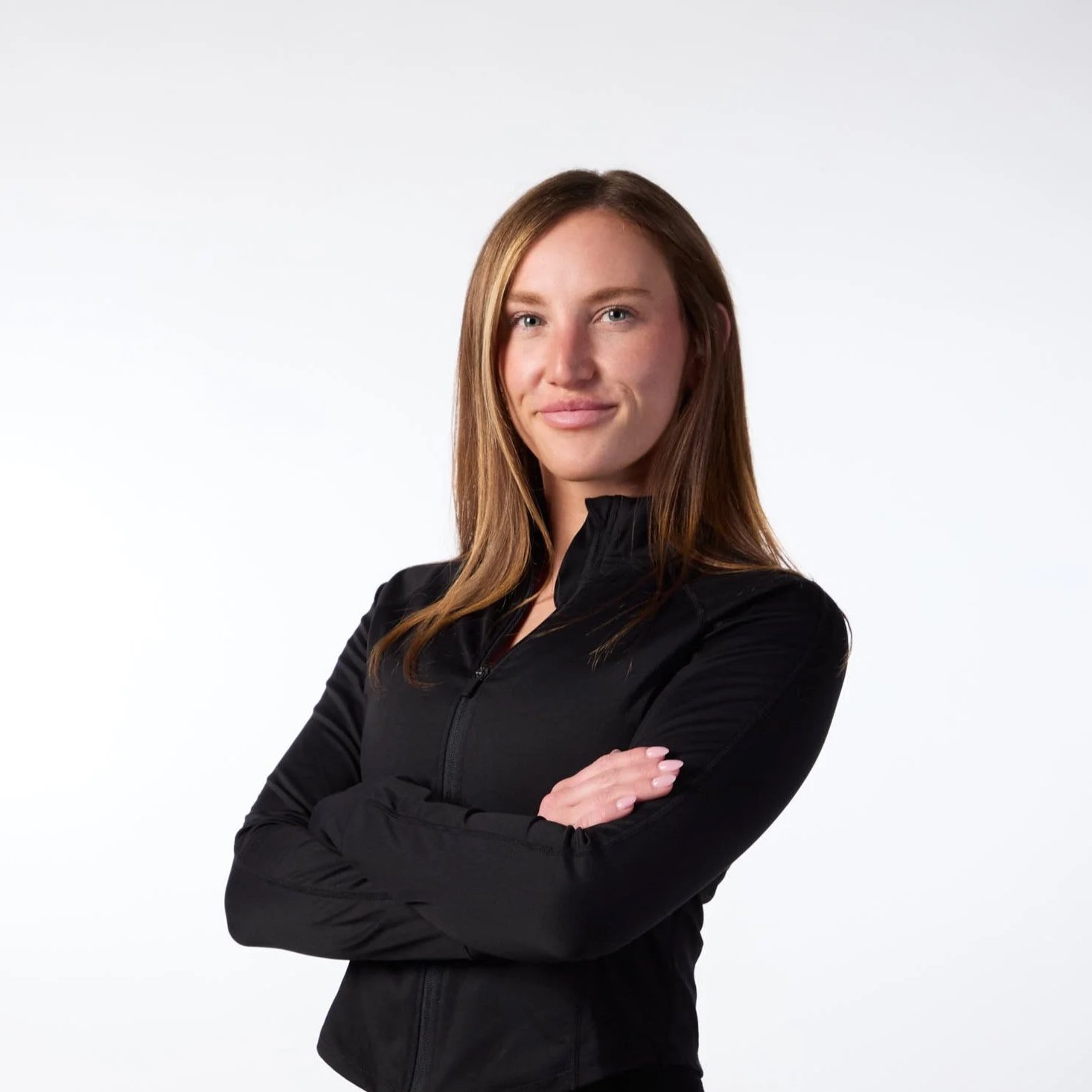 Confident woman with crossed arms wearing a black athletic jacket against a plain white background.
