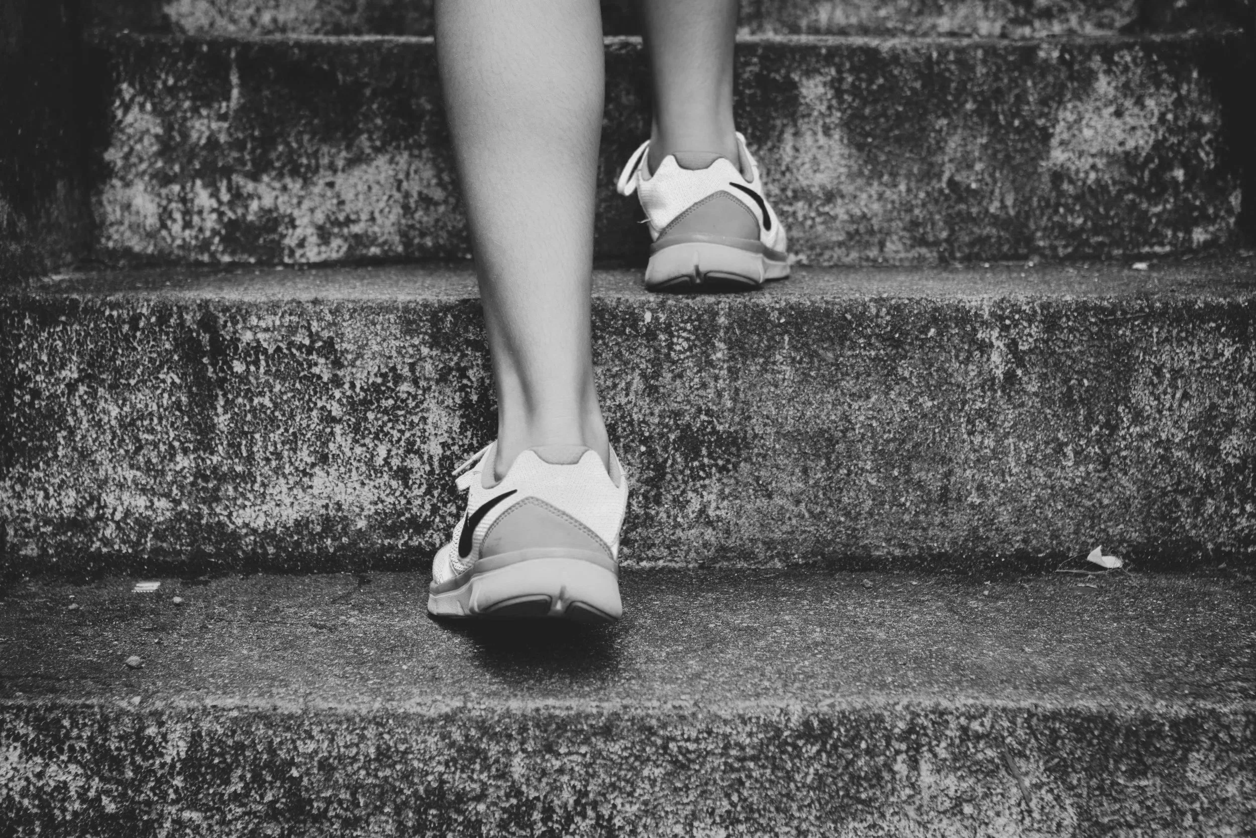 A person wearing sneakers walking up stone stairs.