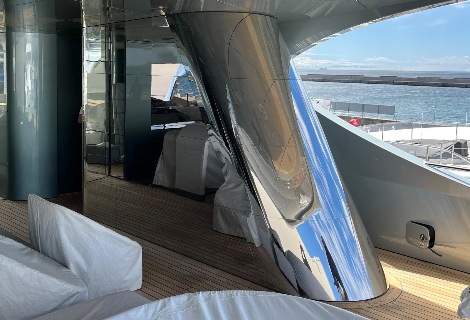 L'interno di uno yacht di lusso con pareti di vetro, sedie bianche e vista sul mare e un molo all'aperto.