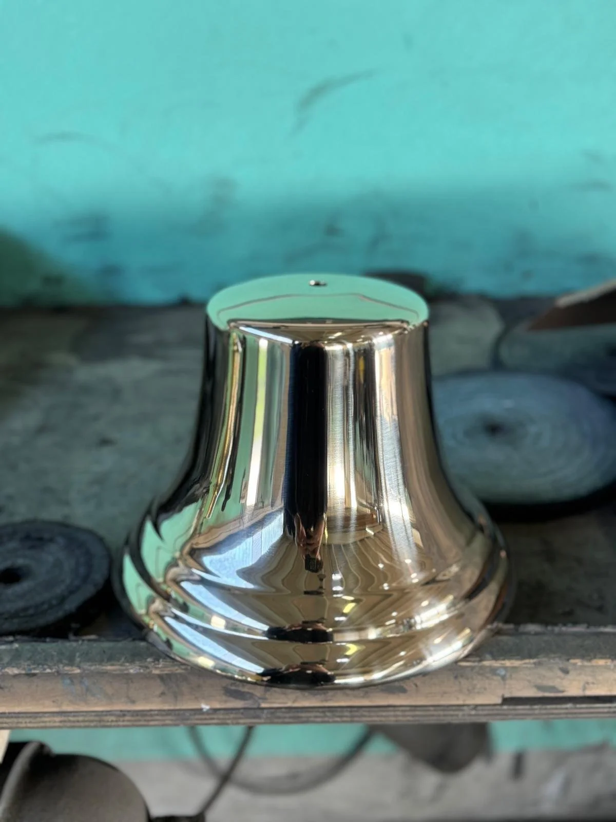 Vaso d'argento riflettente su una superficie di legno con sfondo blu e strumenti di lavorazione del metallo.