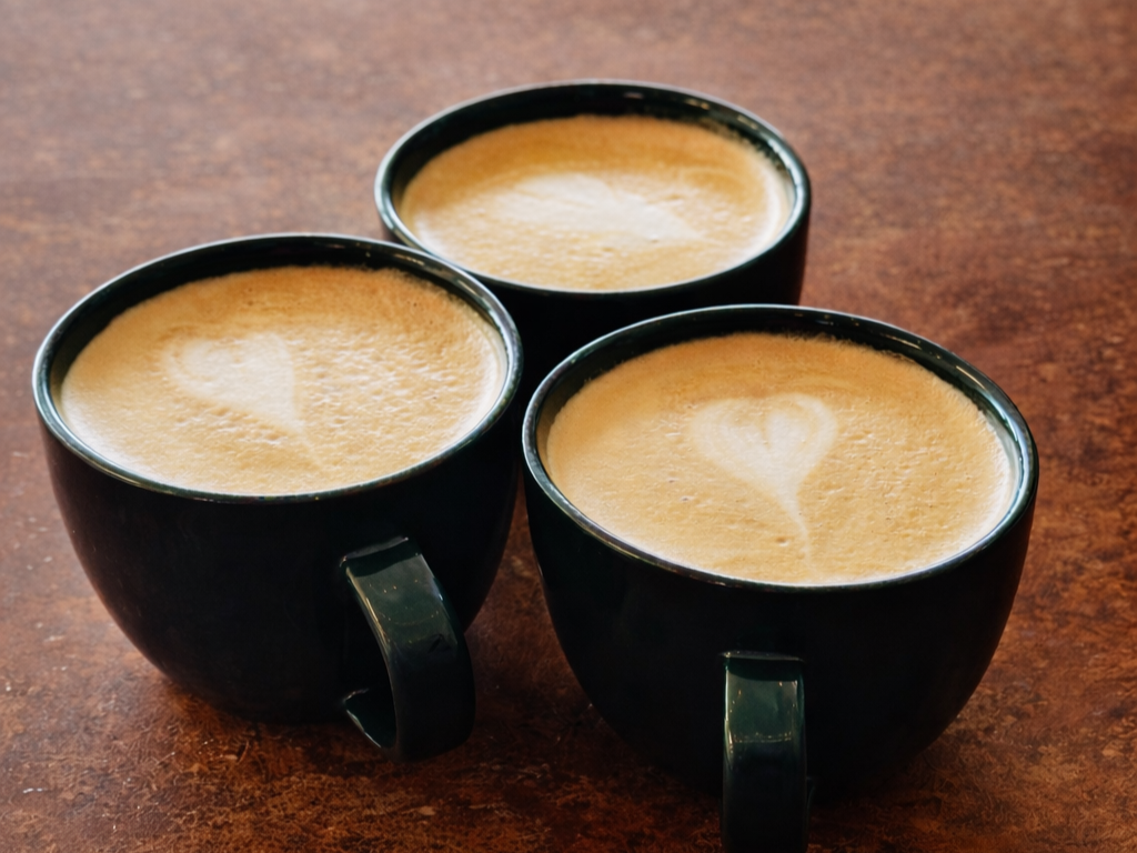 Three cups of coffee with hearts showing in the foam.