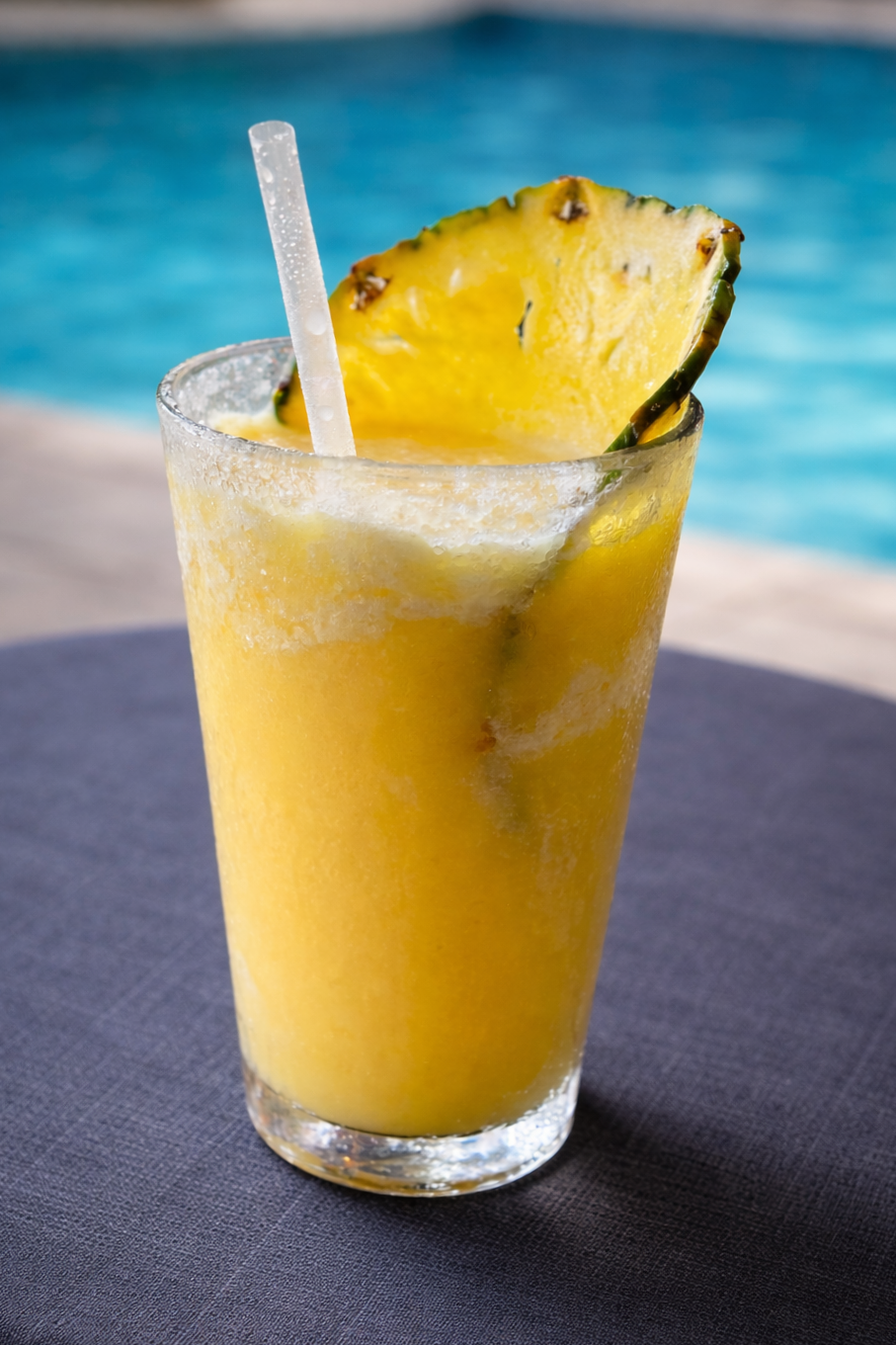 A pineapple drink with a straw by the pool.