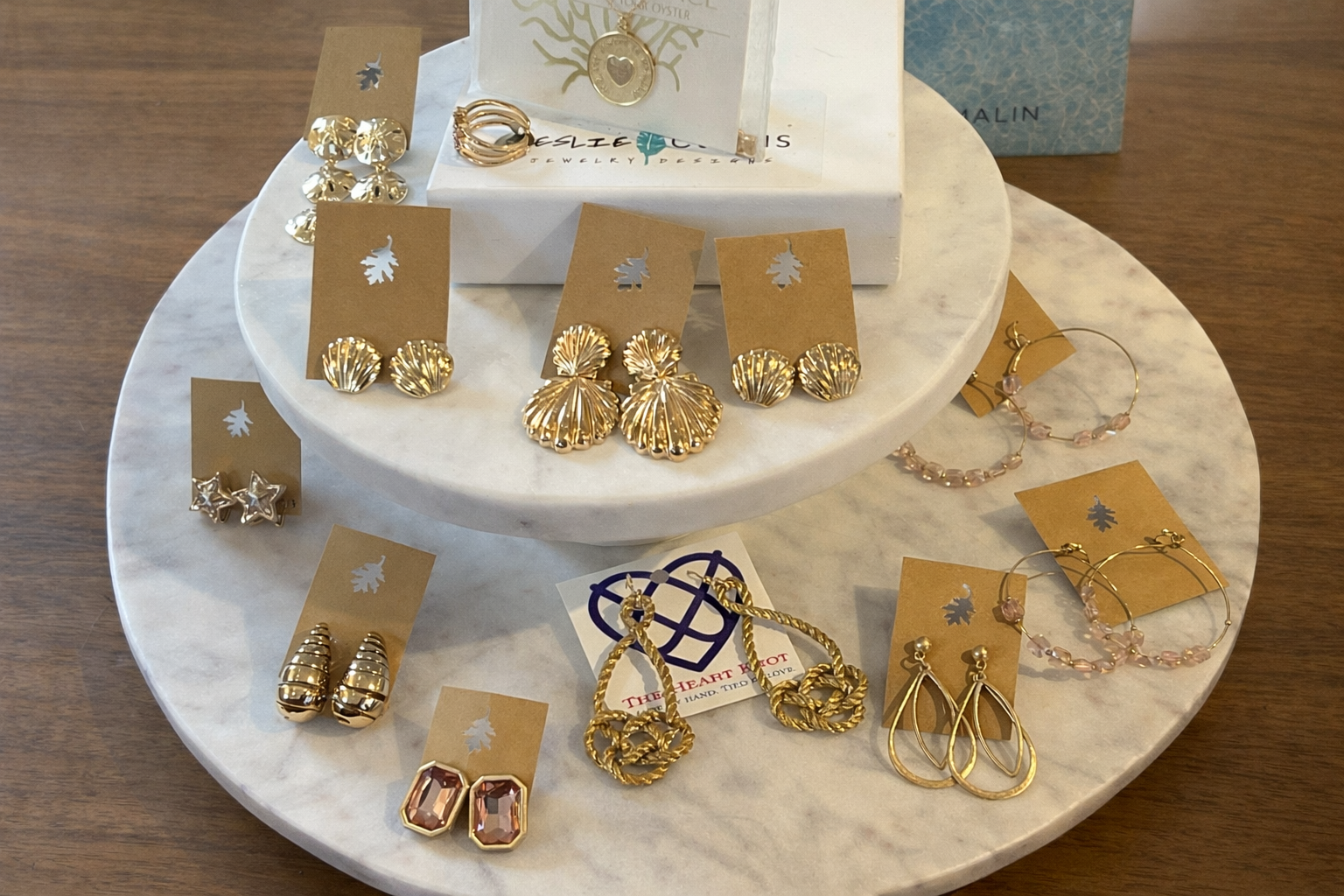 Gold earrings, necklace and ring on two tiered, round marble display plates.