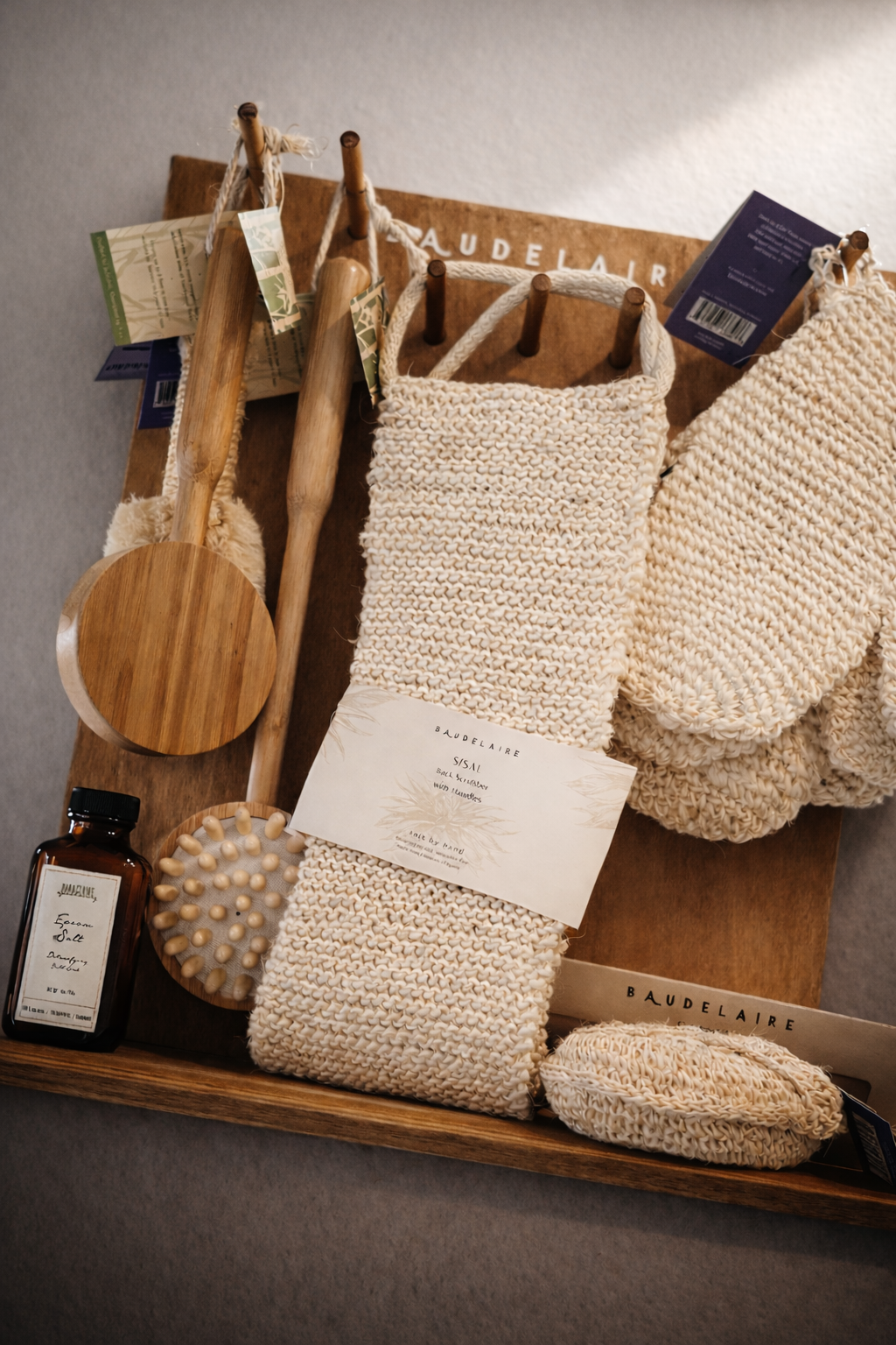 Baudelaire back scrubber with other bath products hanging on a wooden display.