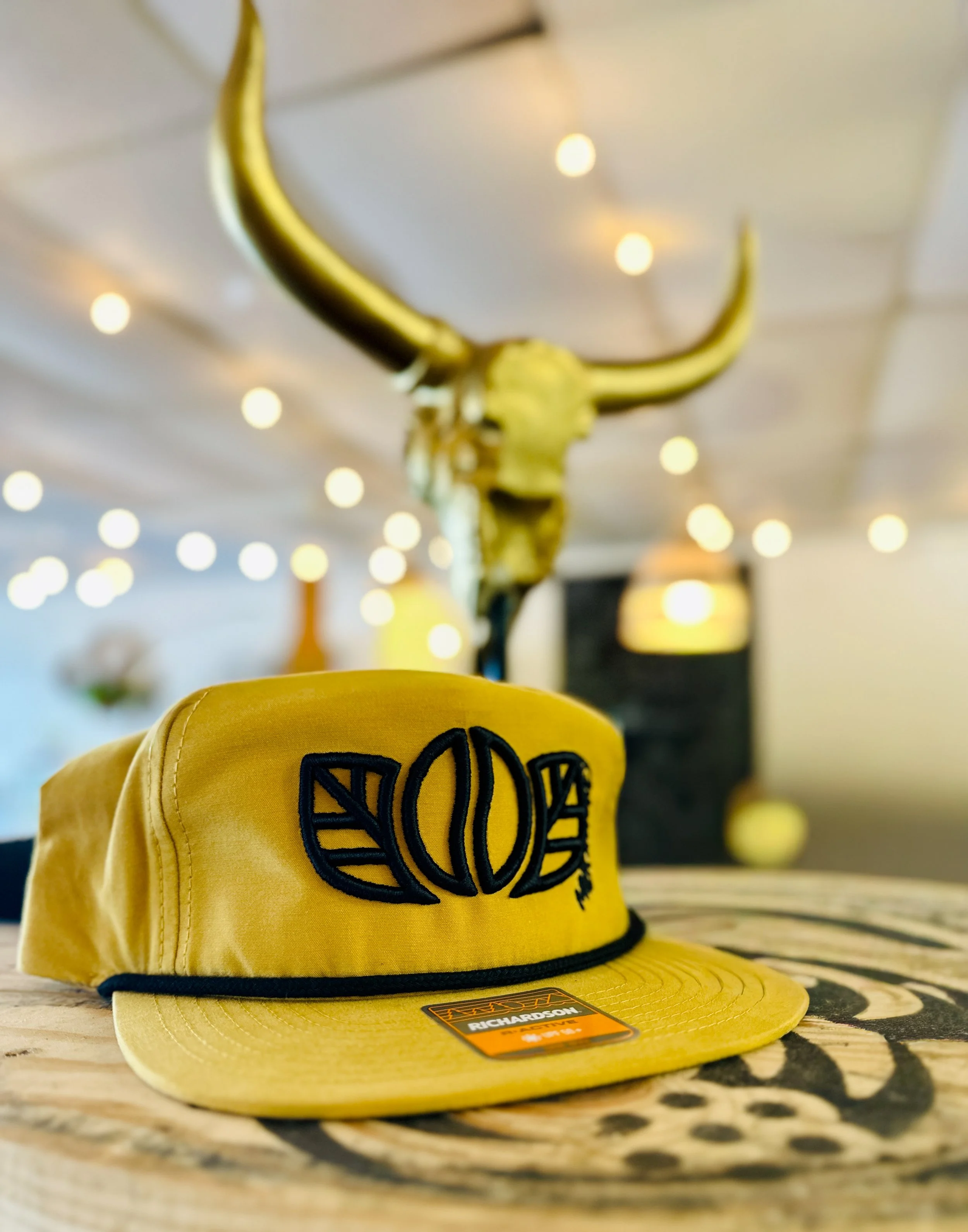 Yellow logo hat on a wood table with golden lights in the background.
