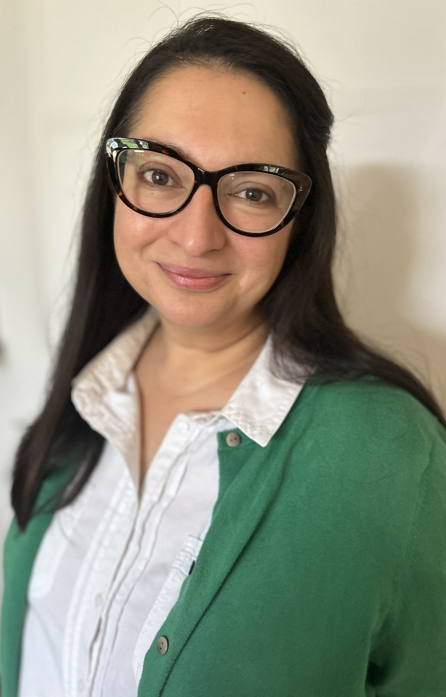 Dr Darrelle: A woman with long dark hair, wearing glasses, a white blouse, and a green cardigan, smiling at the camera.