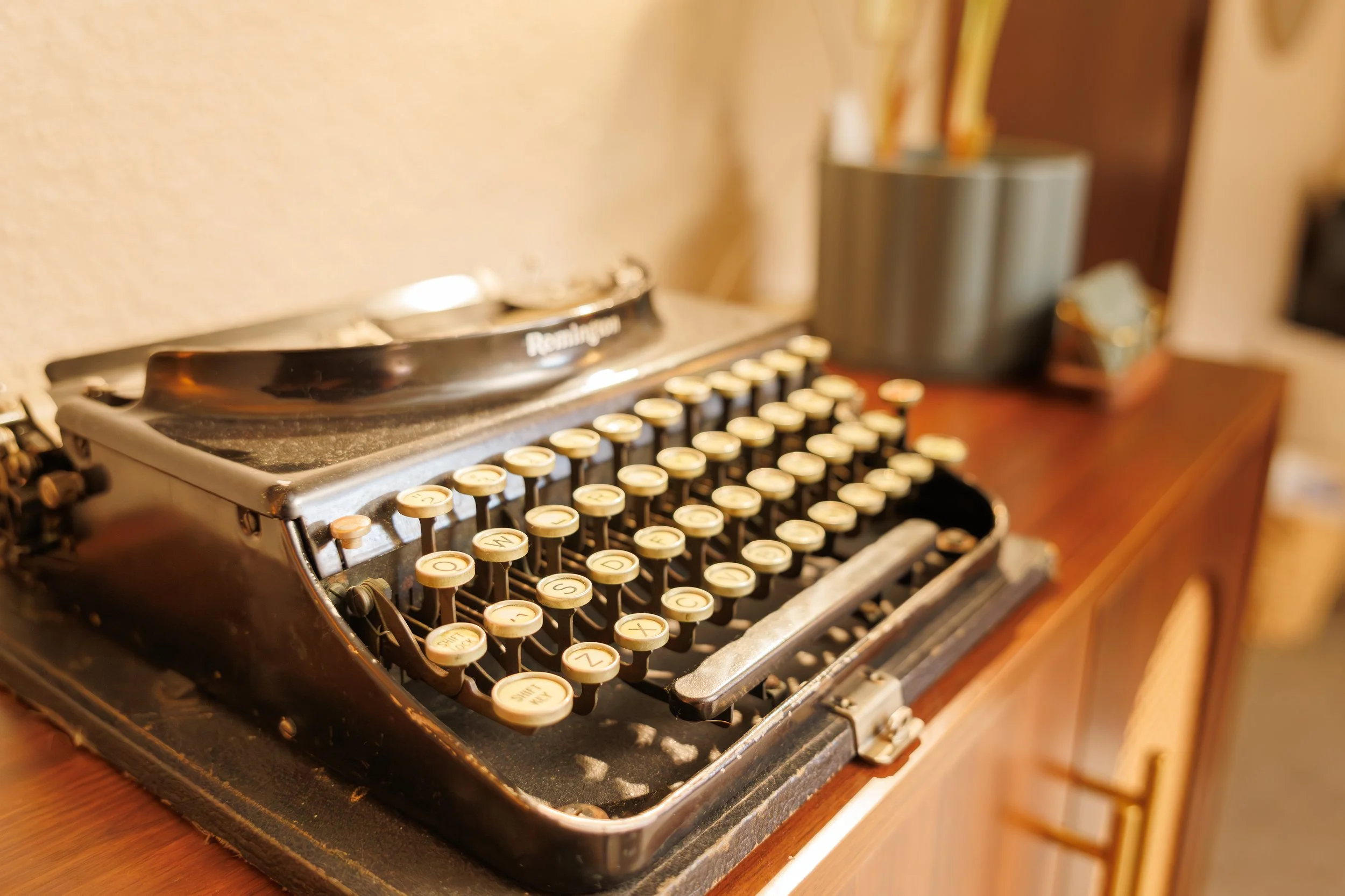 A vintage Remington typewriter with round beige keys, placed on a wooden surface in a room with blurred background.