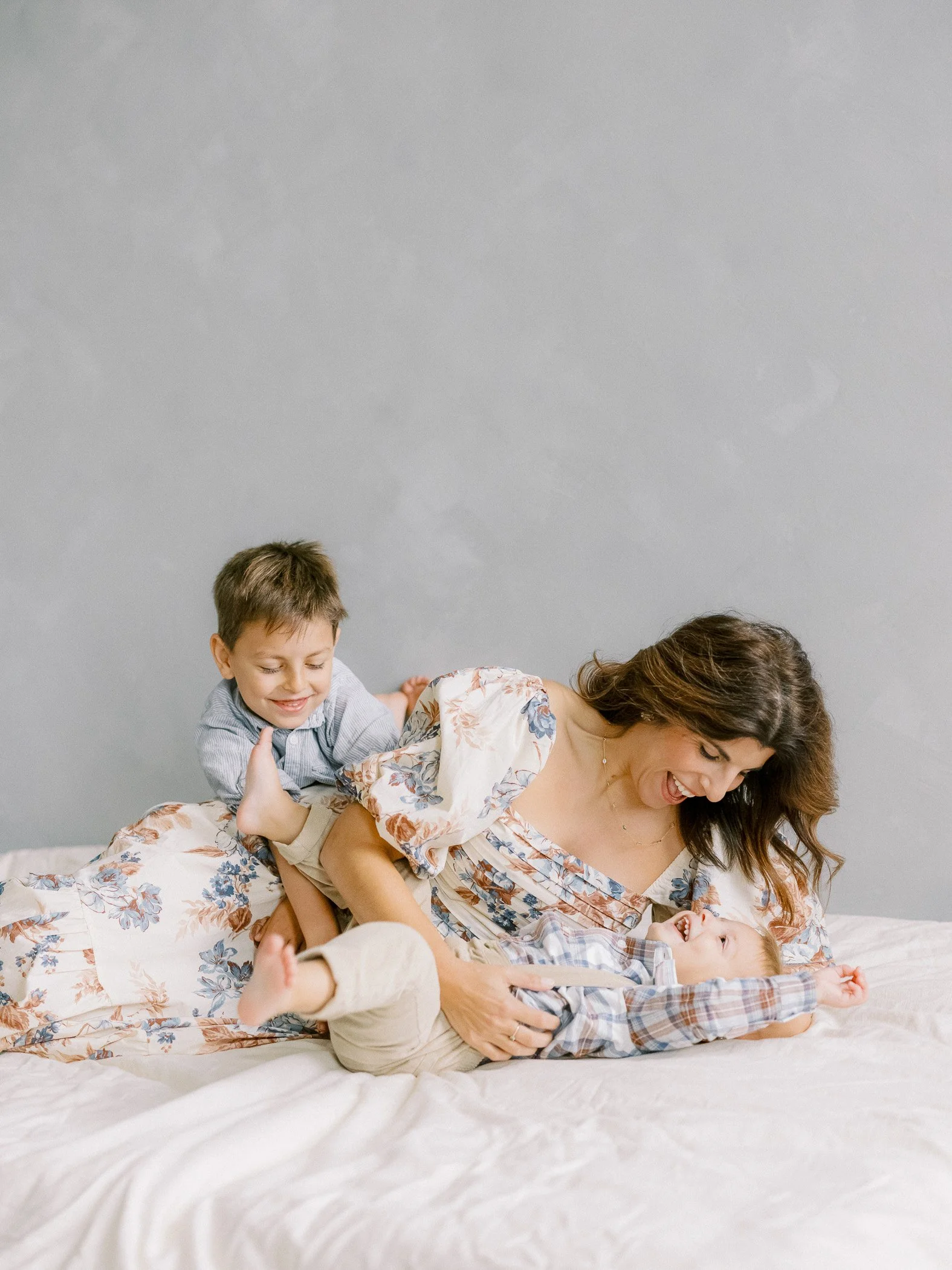 A woman and two young children playing on a bed, laughing and smiling.