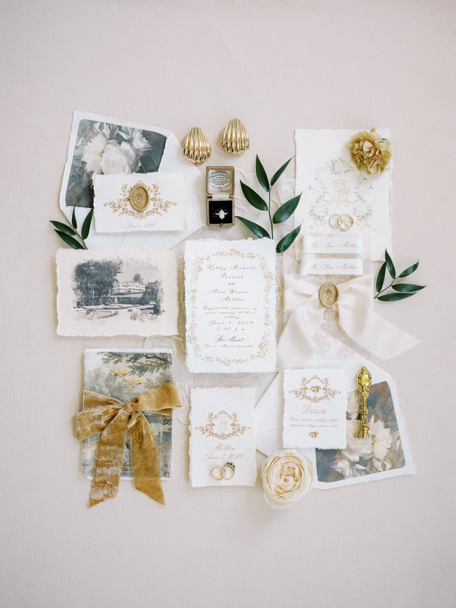 Wedding invitation suite with rings, jewelry, flowers, and decorative paper items arranged on a neutral background.