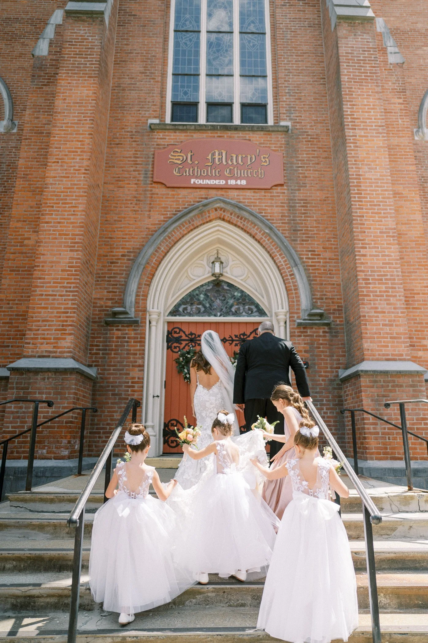 Bride and groom walking up church steps with flower girls in white dresses.